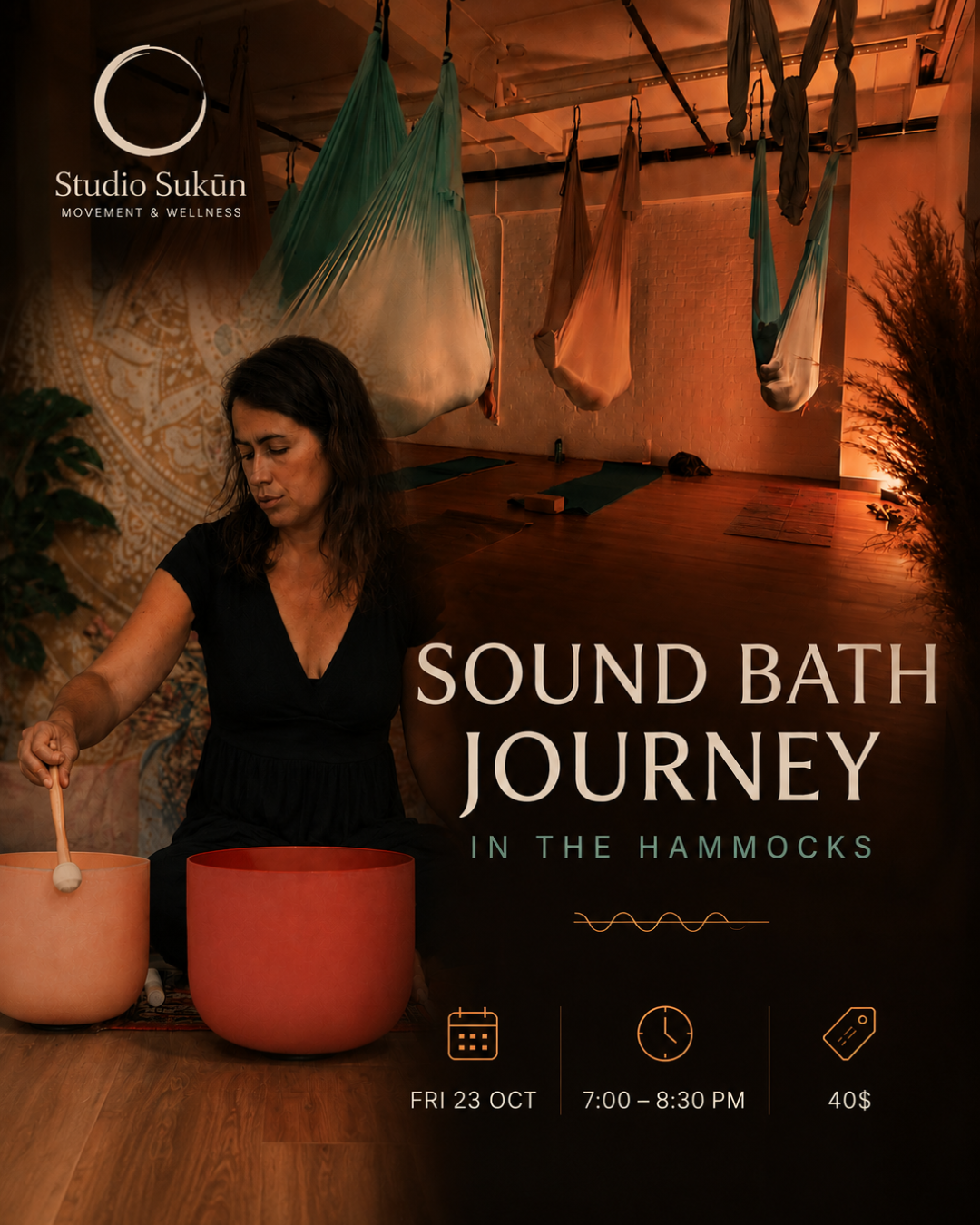 A woman playing a crystal singing bowl during a sound bath session in a warmly lit room with hanging hammocks used for aerial yoga.
