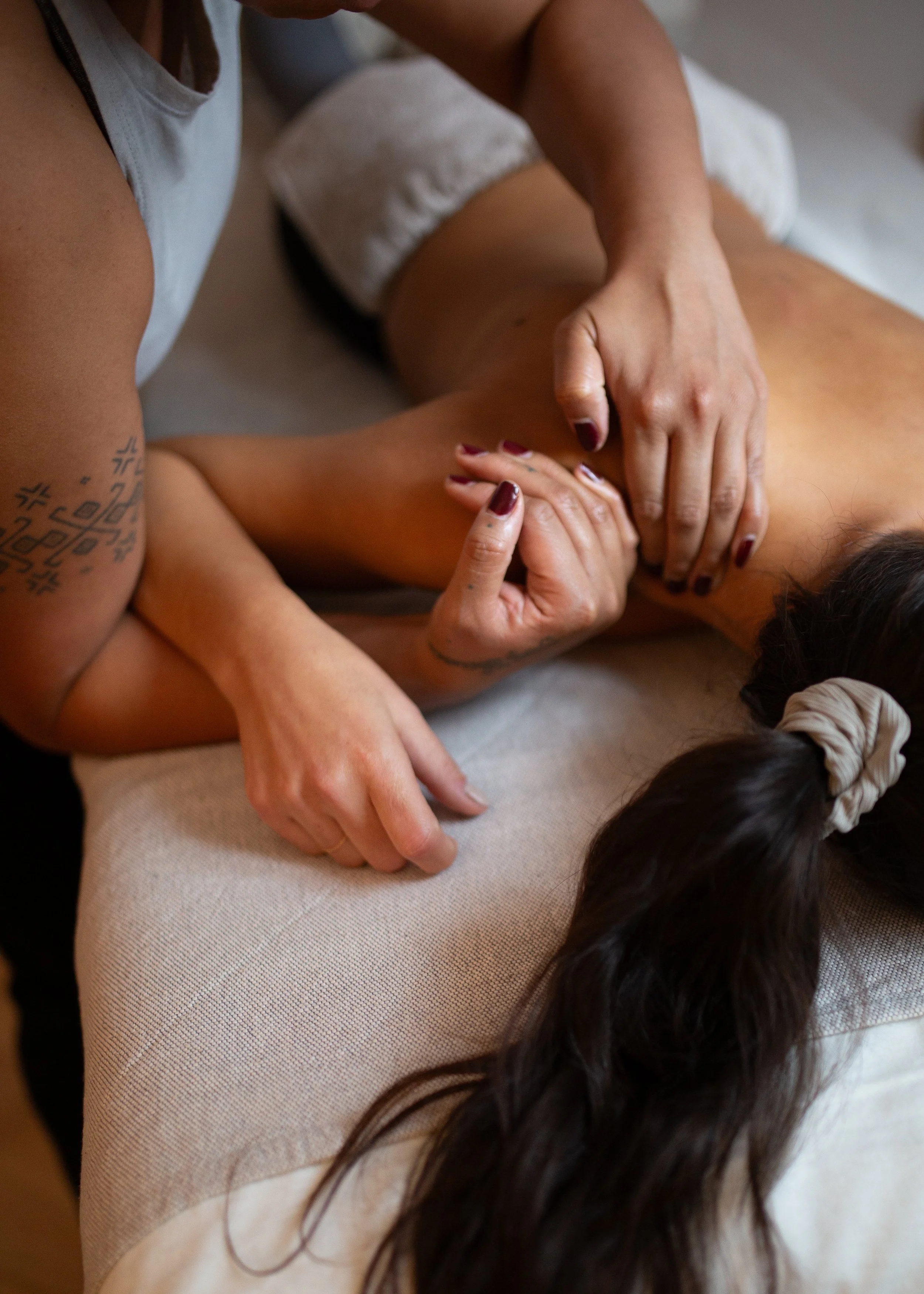 Person giving a massage to another person's shoulder and arm, on a beige towel with a person's dark hair visible at the bottom of the image.