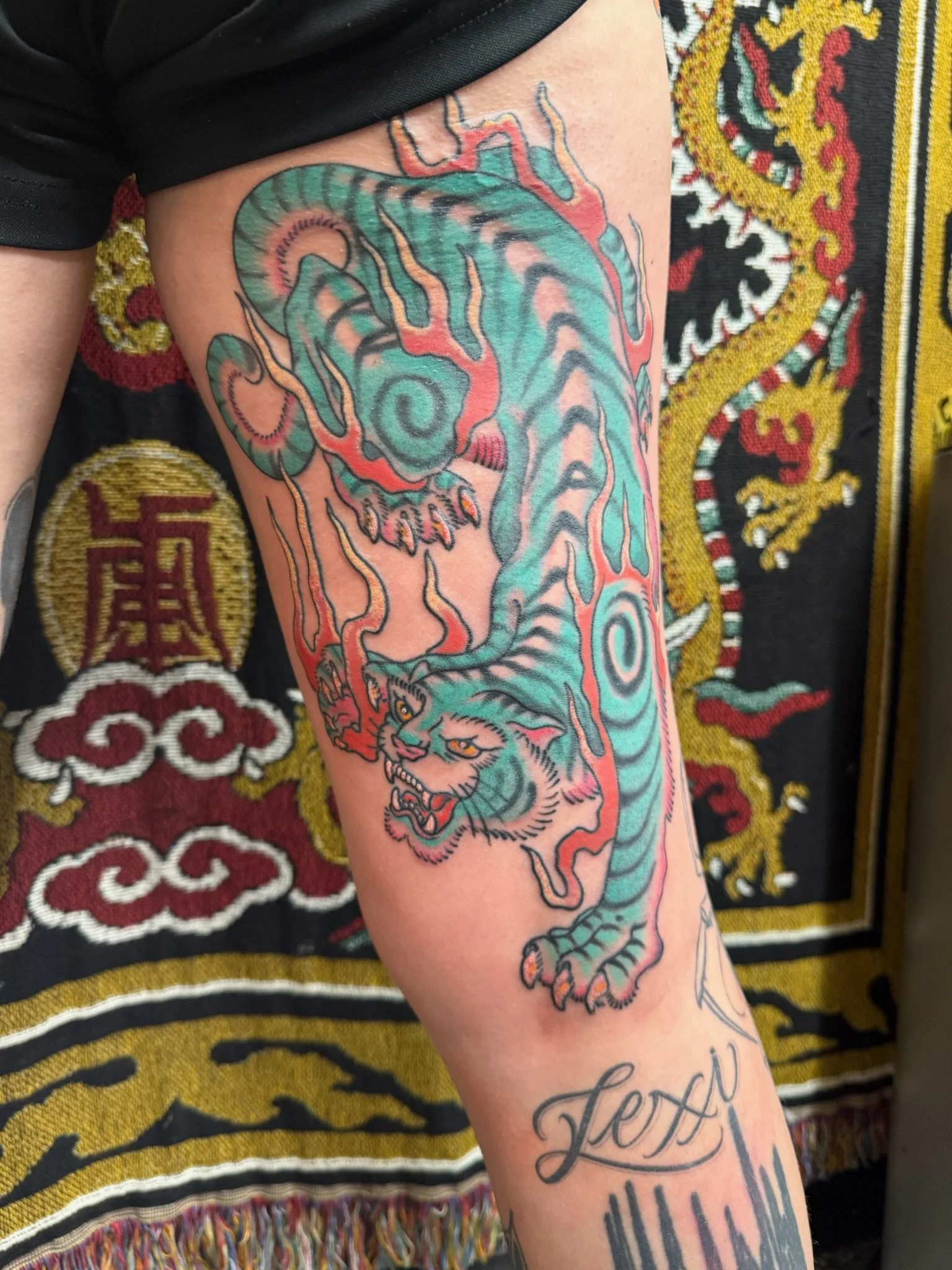 A colorful tattoo of a tiger's head with flames on a person's forearm, featuring intricate details and bold colors.