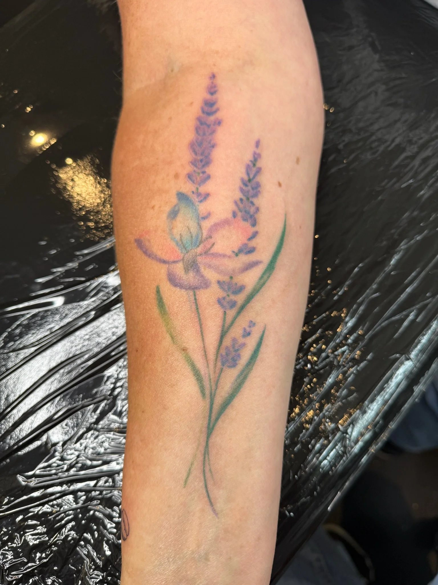 A tattoo of lavender flowers with green stems on a person's forearm.