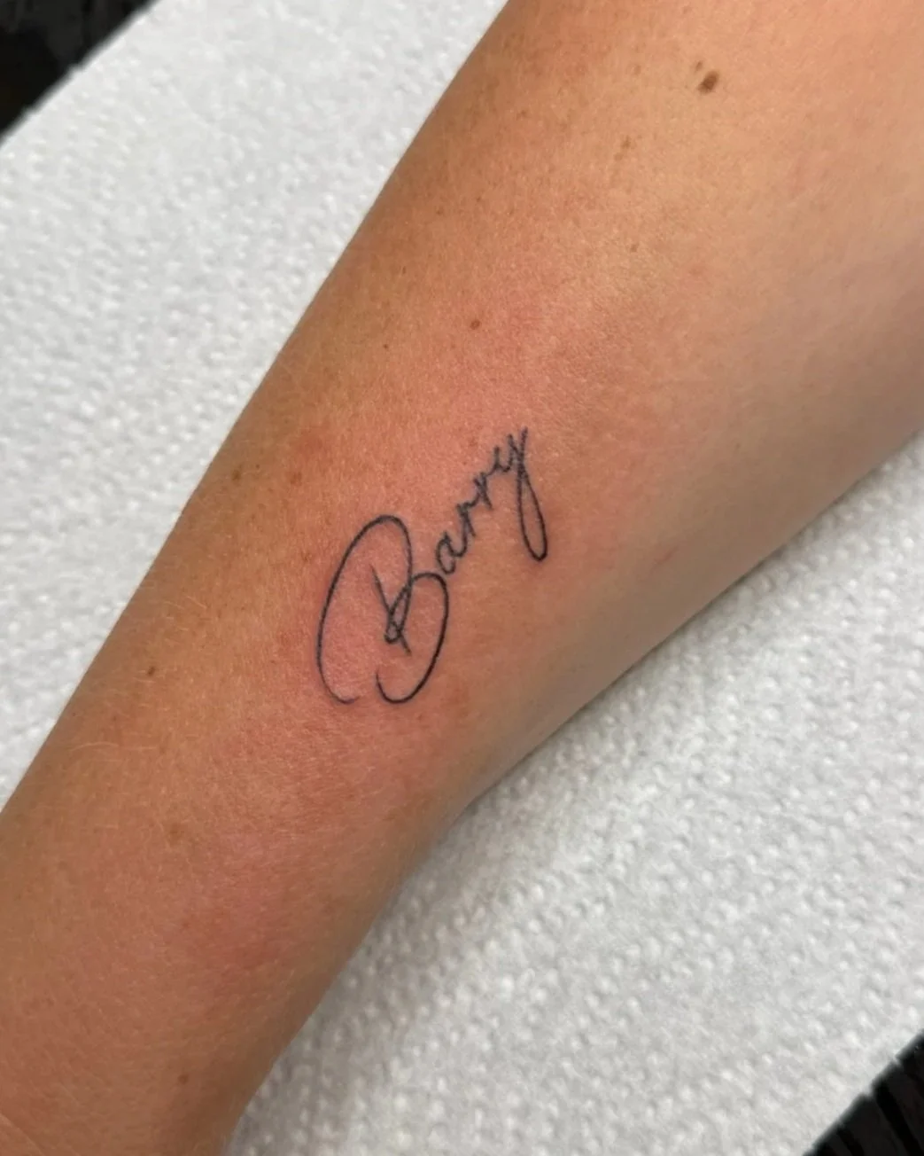 A tattoo of the word 'Barry' in cursive on a person's forearm.