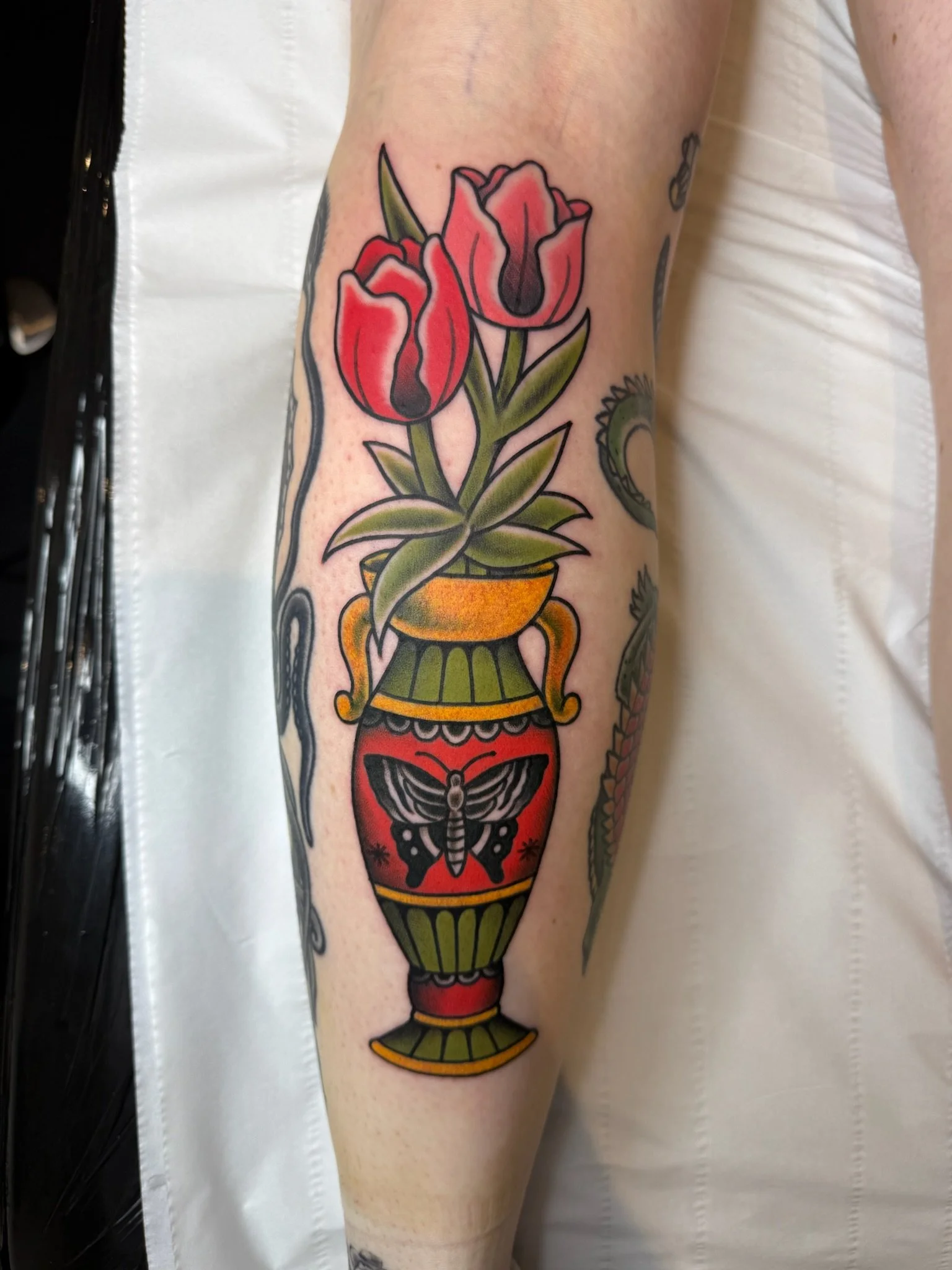 Colorful tattoo of a vase with three red tulips on a person's forearm.
