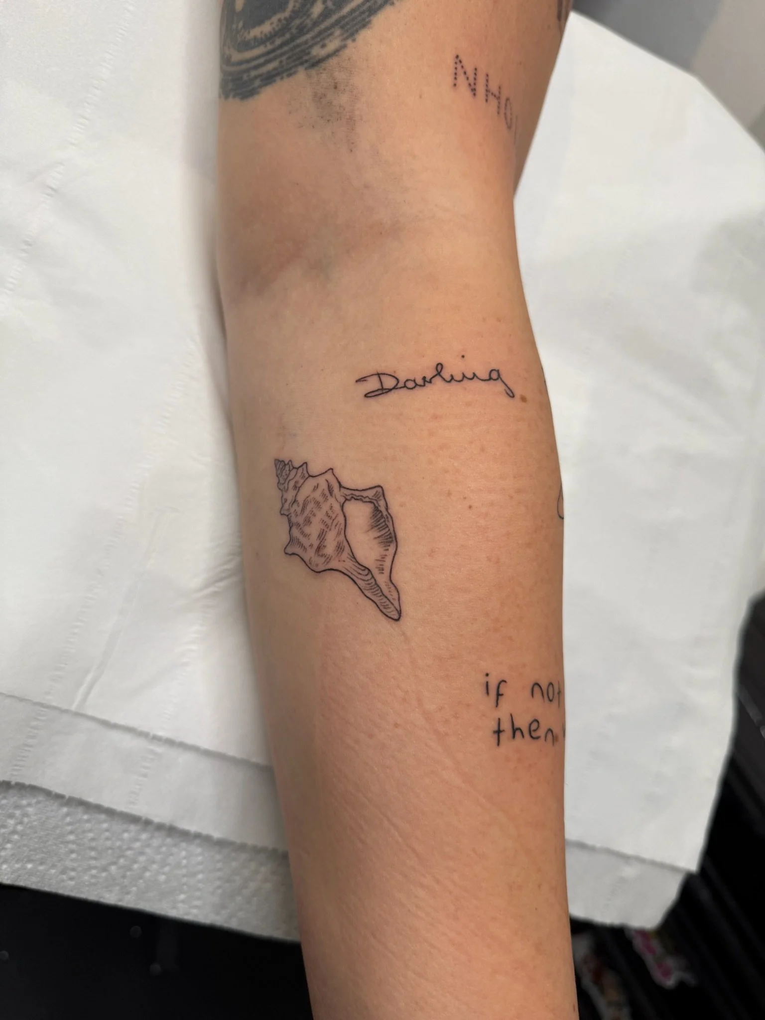 Close-up of a person's arm with multiple tattoos, including the word 'Darling' in cursive, an outlined map of Puerto Rico, and some partially visible script text below.