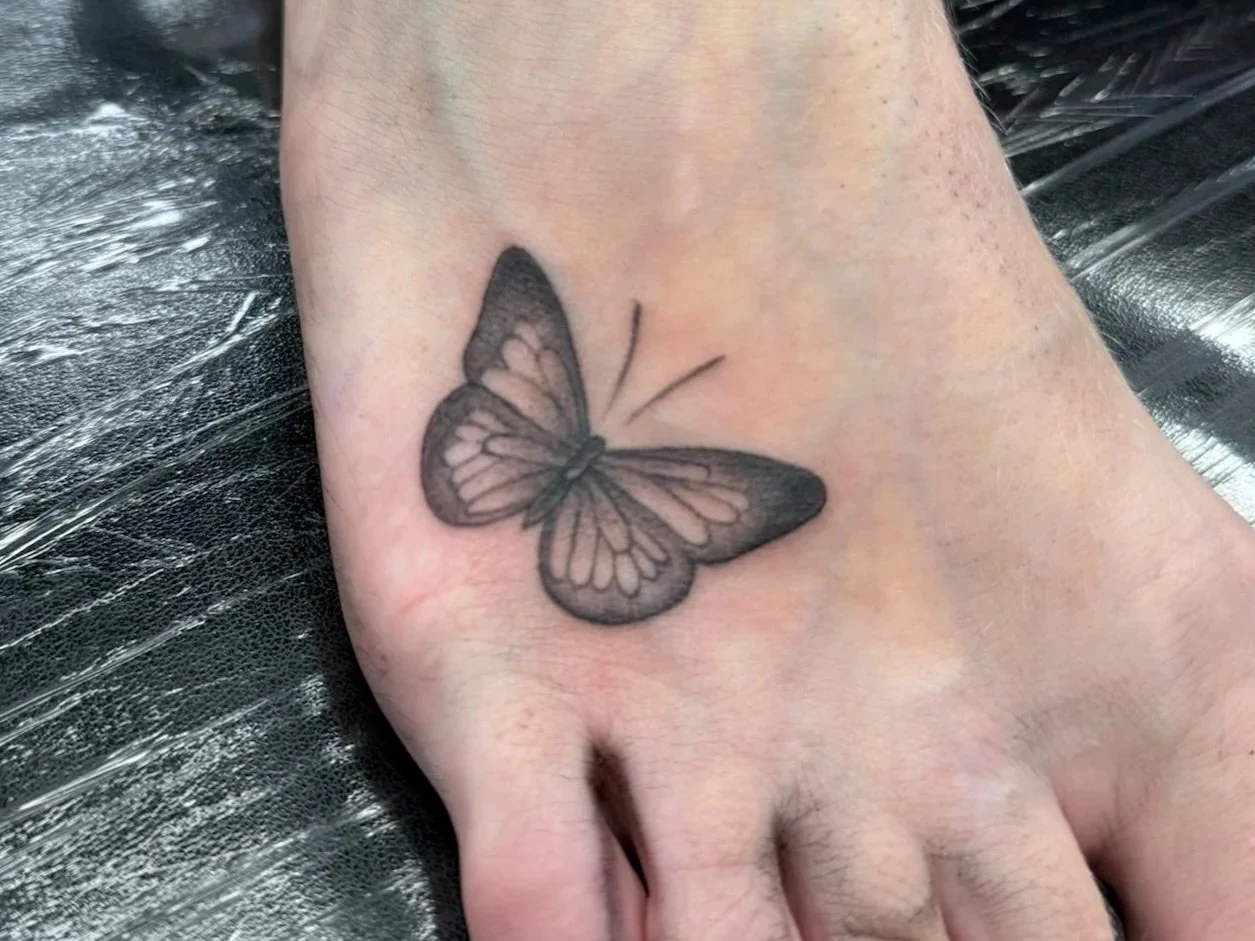 Black and gray butterfly tattoo on a person's hand.