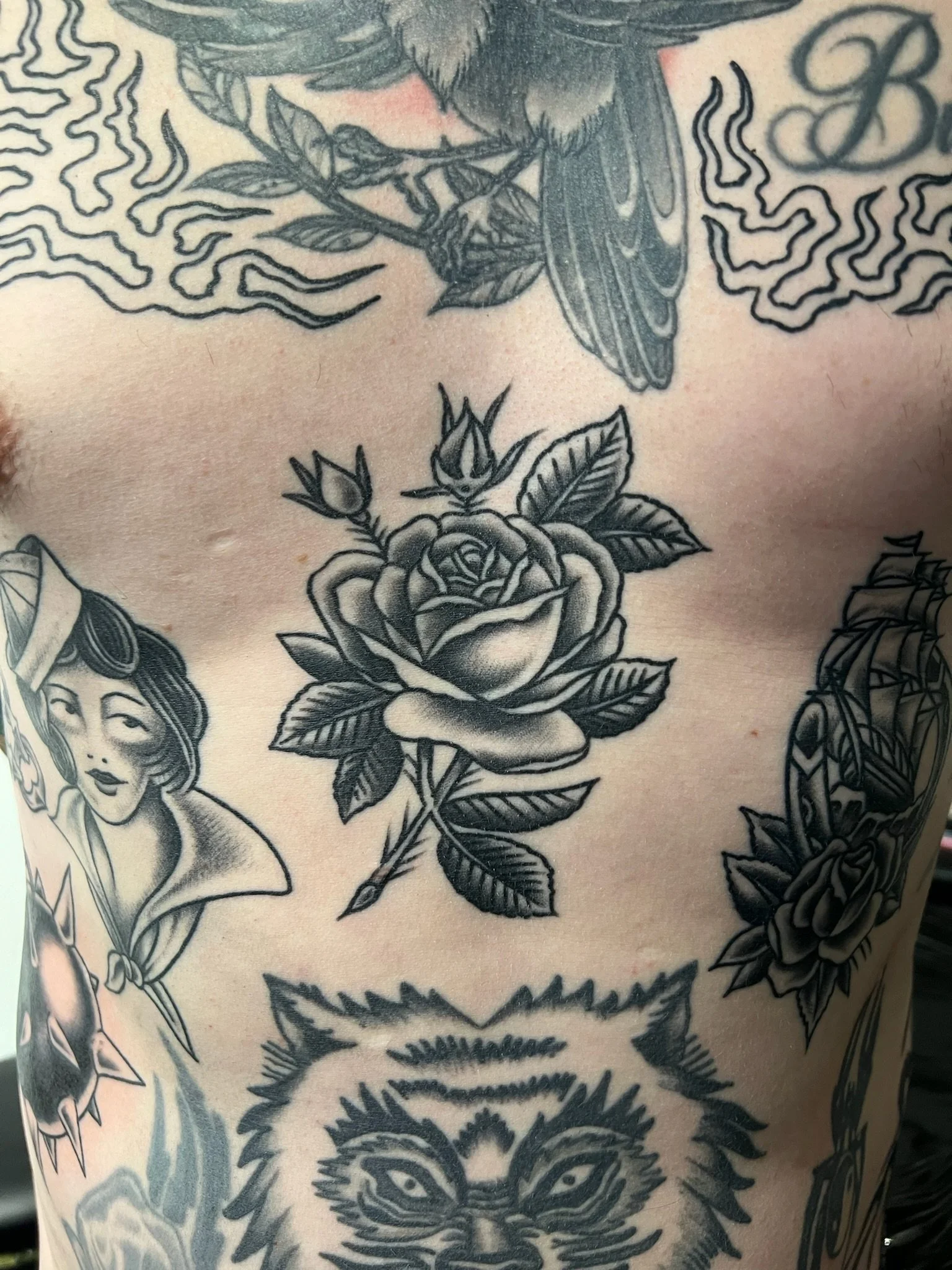Close-up of a tattoo featuring a rose flower and a woman's face with earrings, part of a larger design on skin.