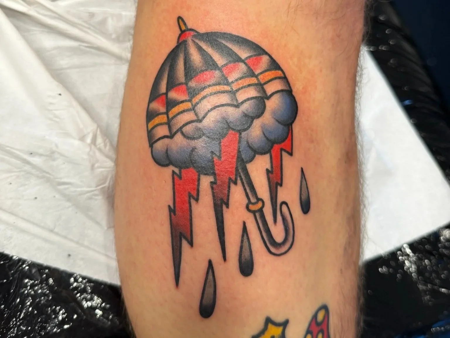 Tattoo of an umbrella with dark clouds and lightning bolts, rain drops, and lightning strikes, in traditional tattoo style.