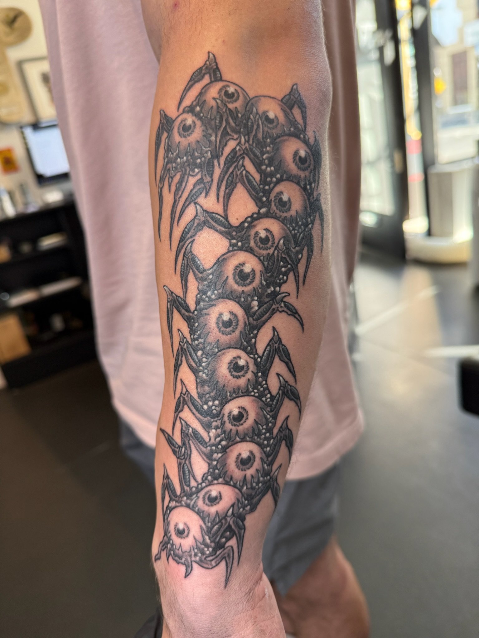 Tattoo of a row of eyes with spider-like legs on a person's forearm.
