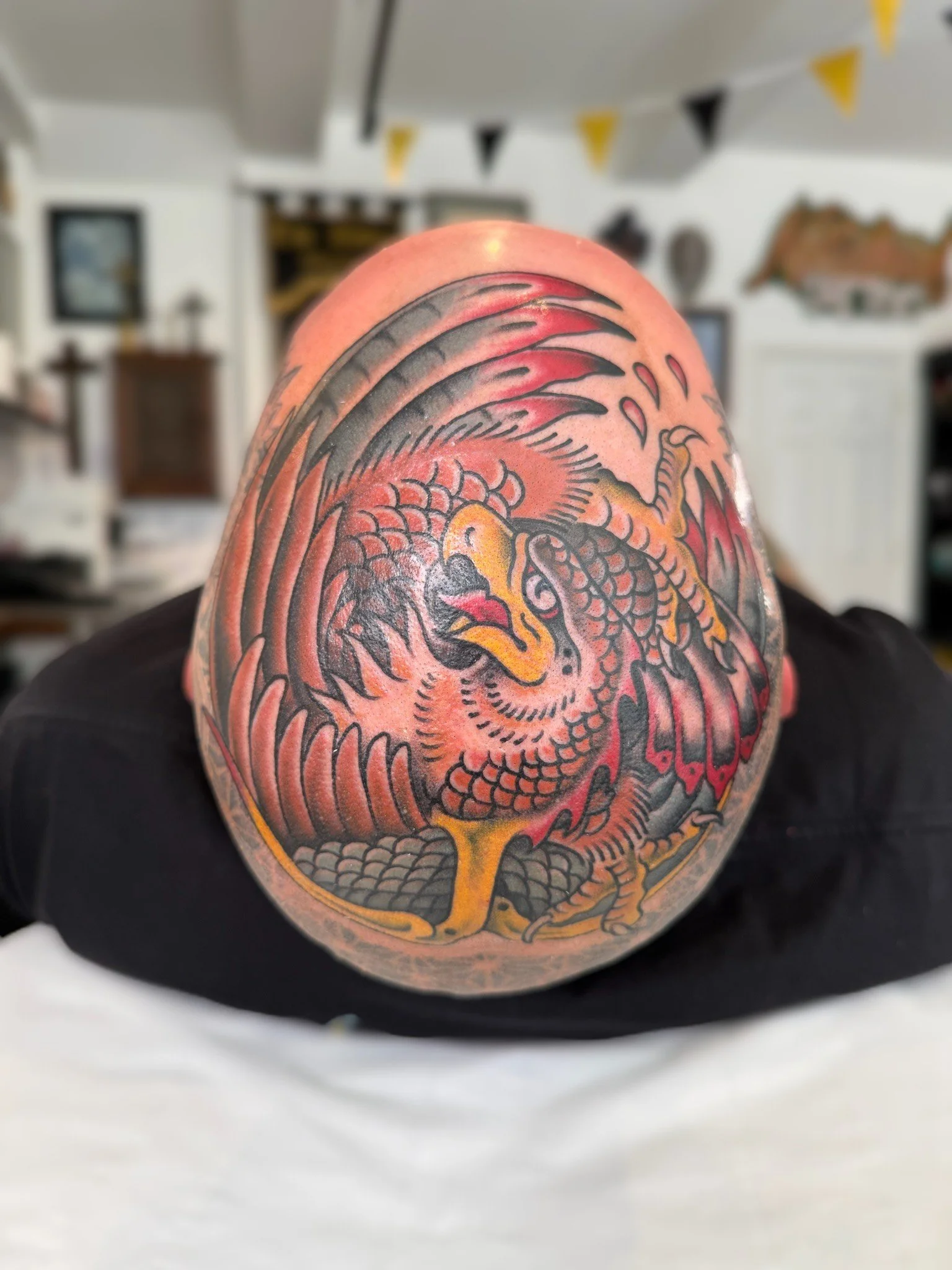 Tattoo of a dragon on a person's shoulder, featuring bold black outlines, red accents, and yellow highlights.