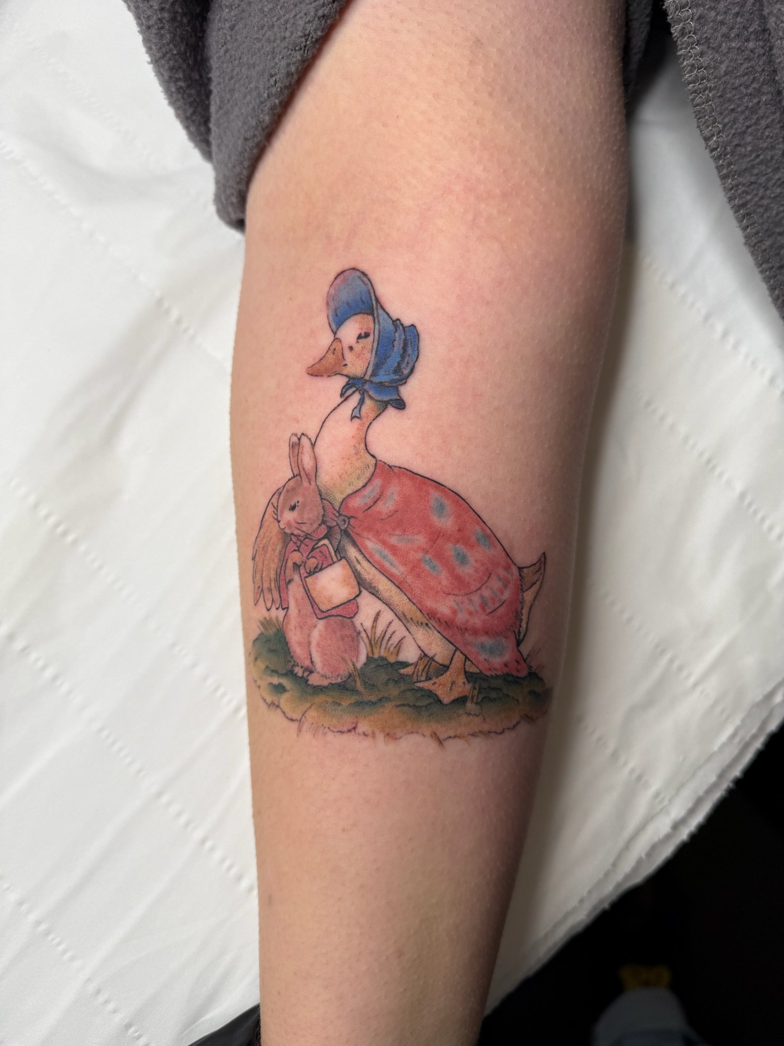 Tattoo of a rabbit with a hat and holding a glass, sitting on grass.