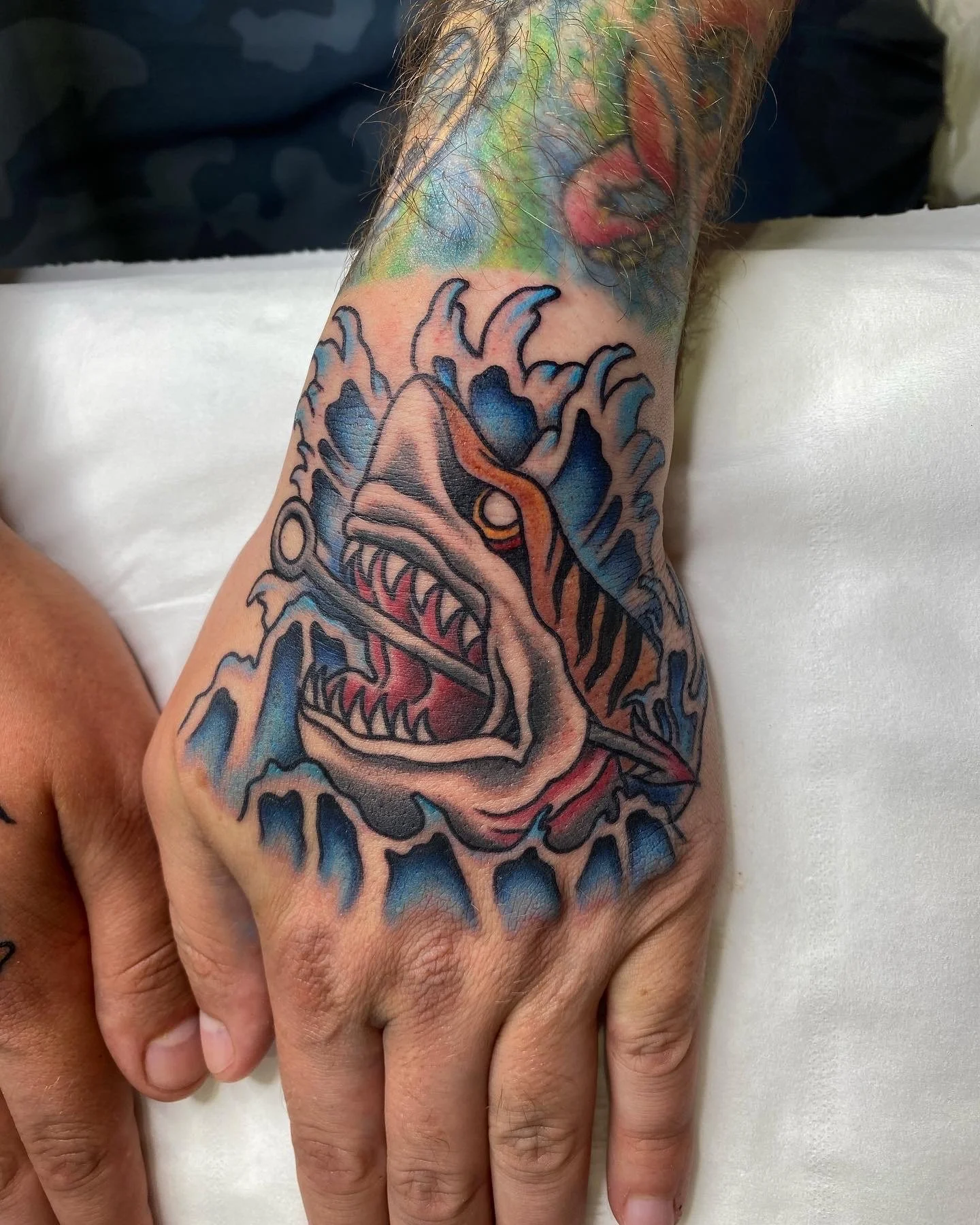 A colorful tattoo of a dinosaur with sharp teeth and a fierce expression on a person's forearm.