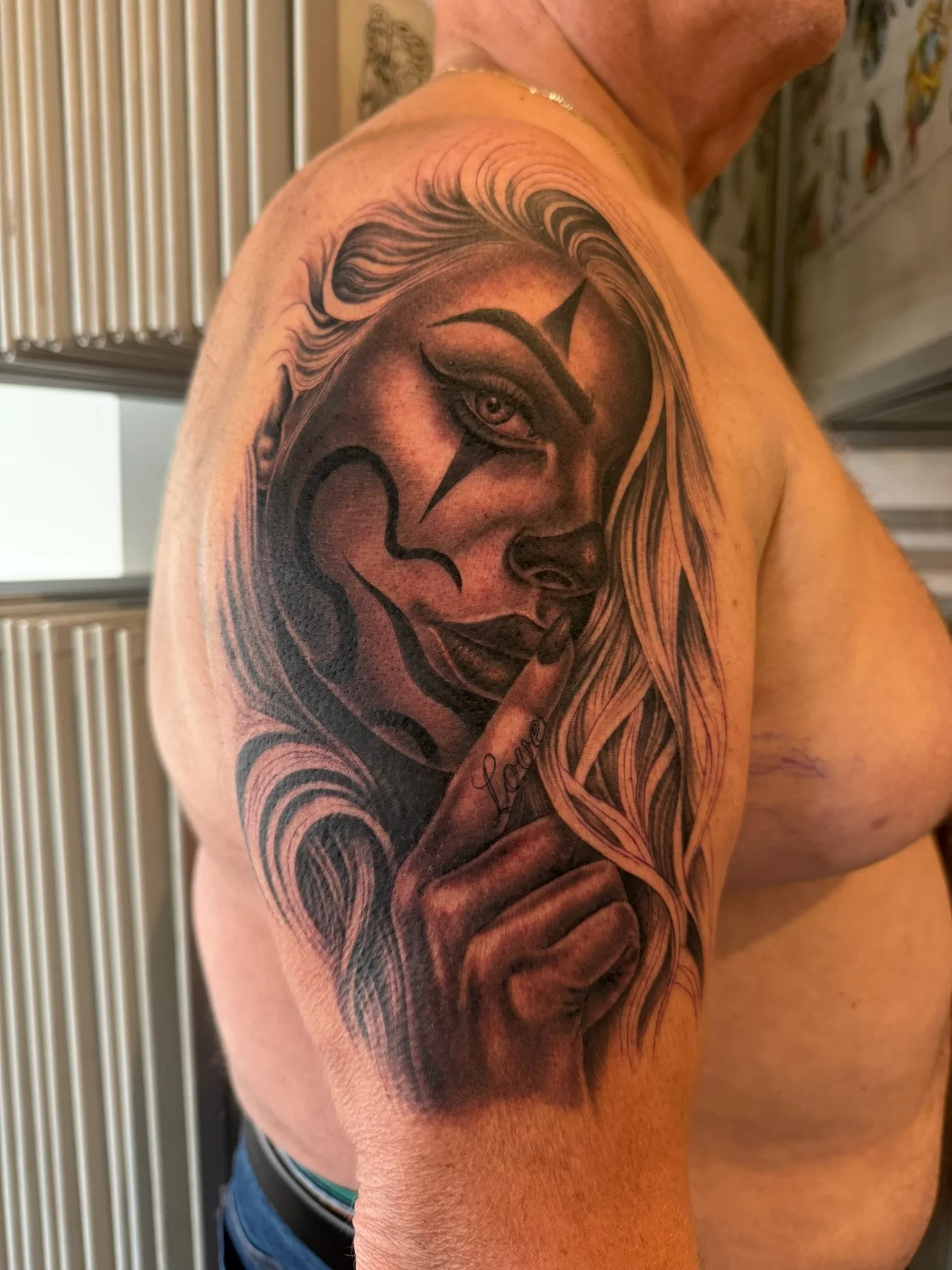 Close-up of a man's shoulder with a detailed black and grey tattoo of a woman's face with flowing hair.