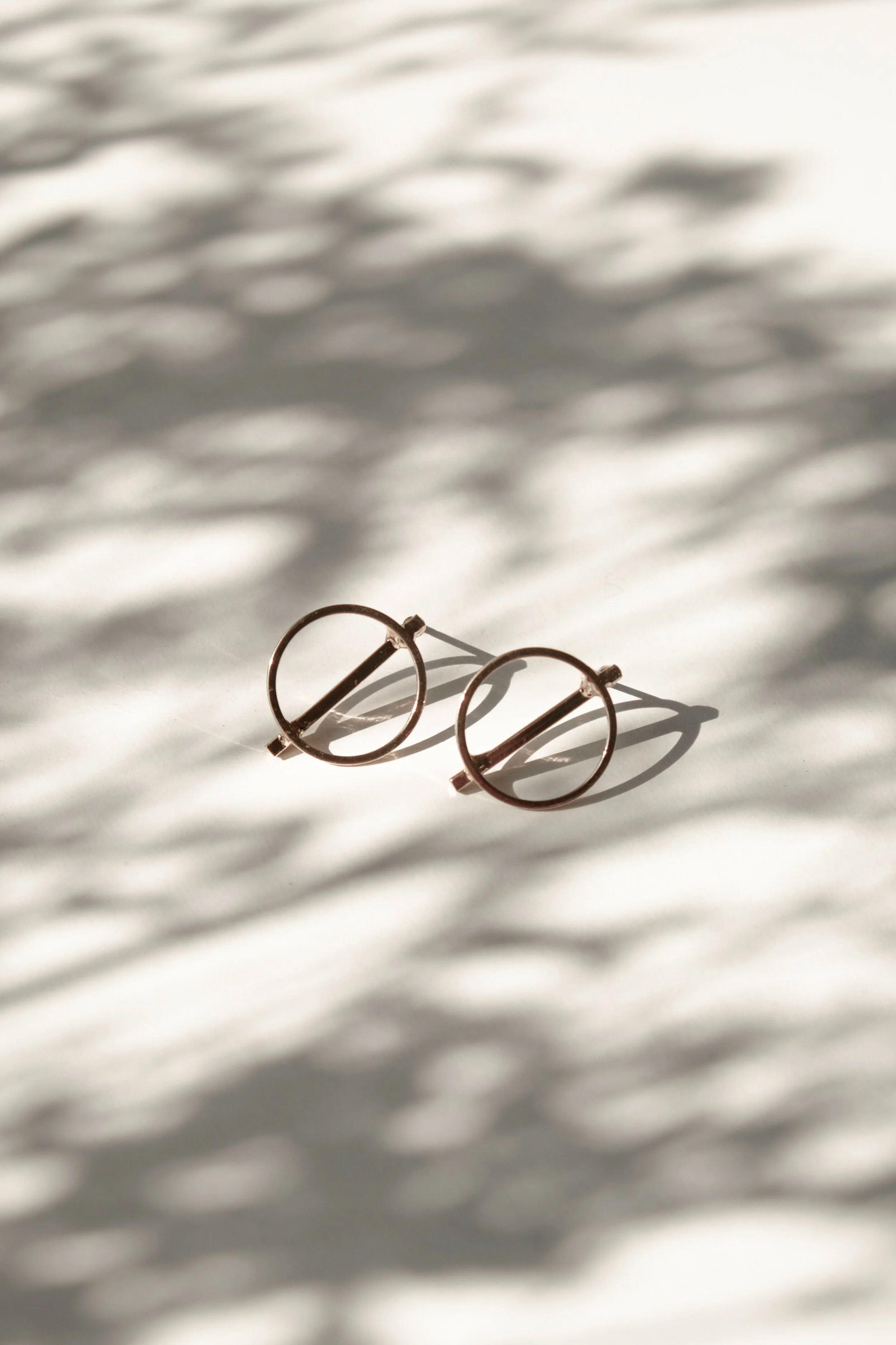 A pair of gold metal eyeglasses resting on a surface with shadows cast by a source of light, creating a pattern on the surface.