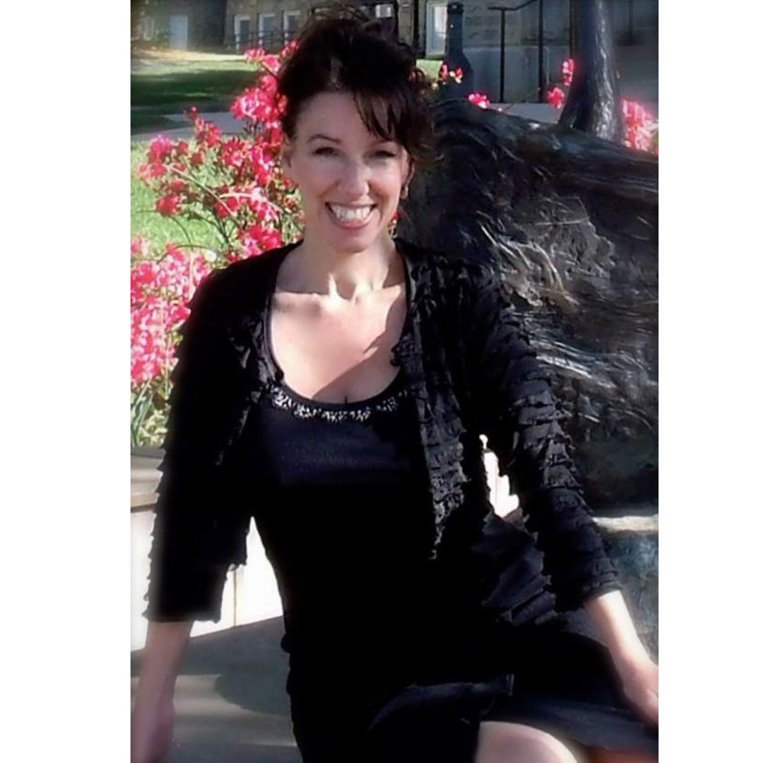 A woman smiling outdoors sitting on a bench with pink flowers in the background.