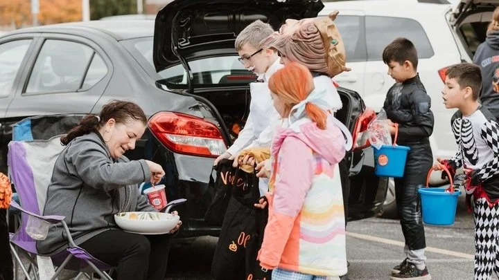 Children with treat buckets gathering beside a decorated car trunk.