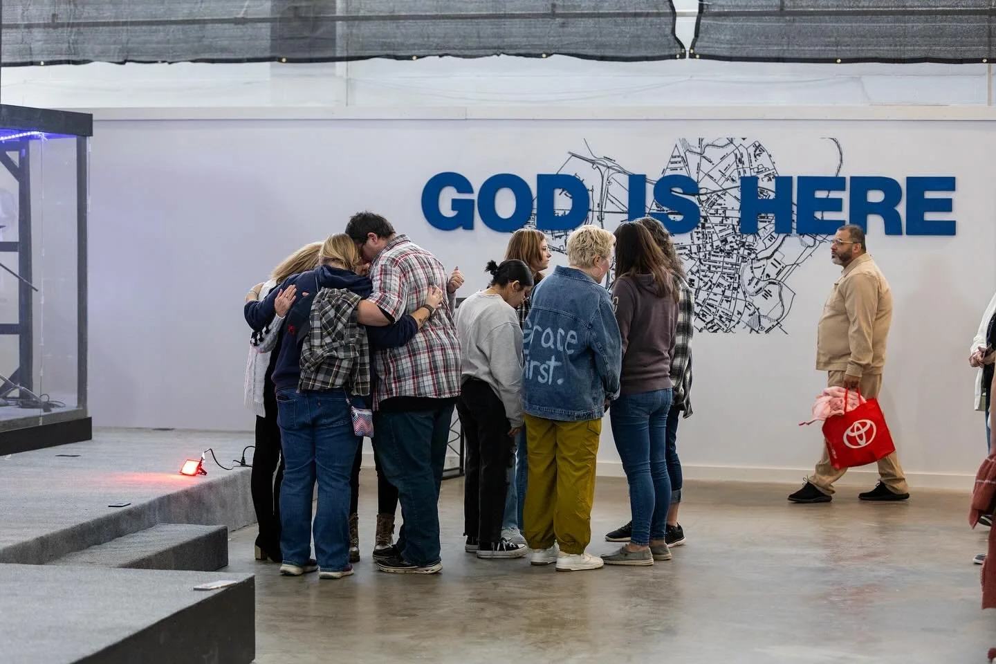People embracing beneath the God Is Here sign at Altered Church.
