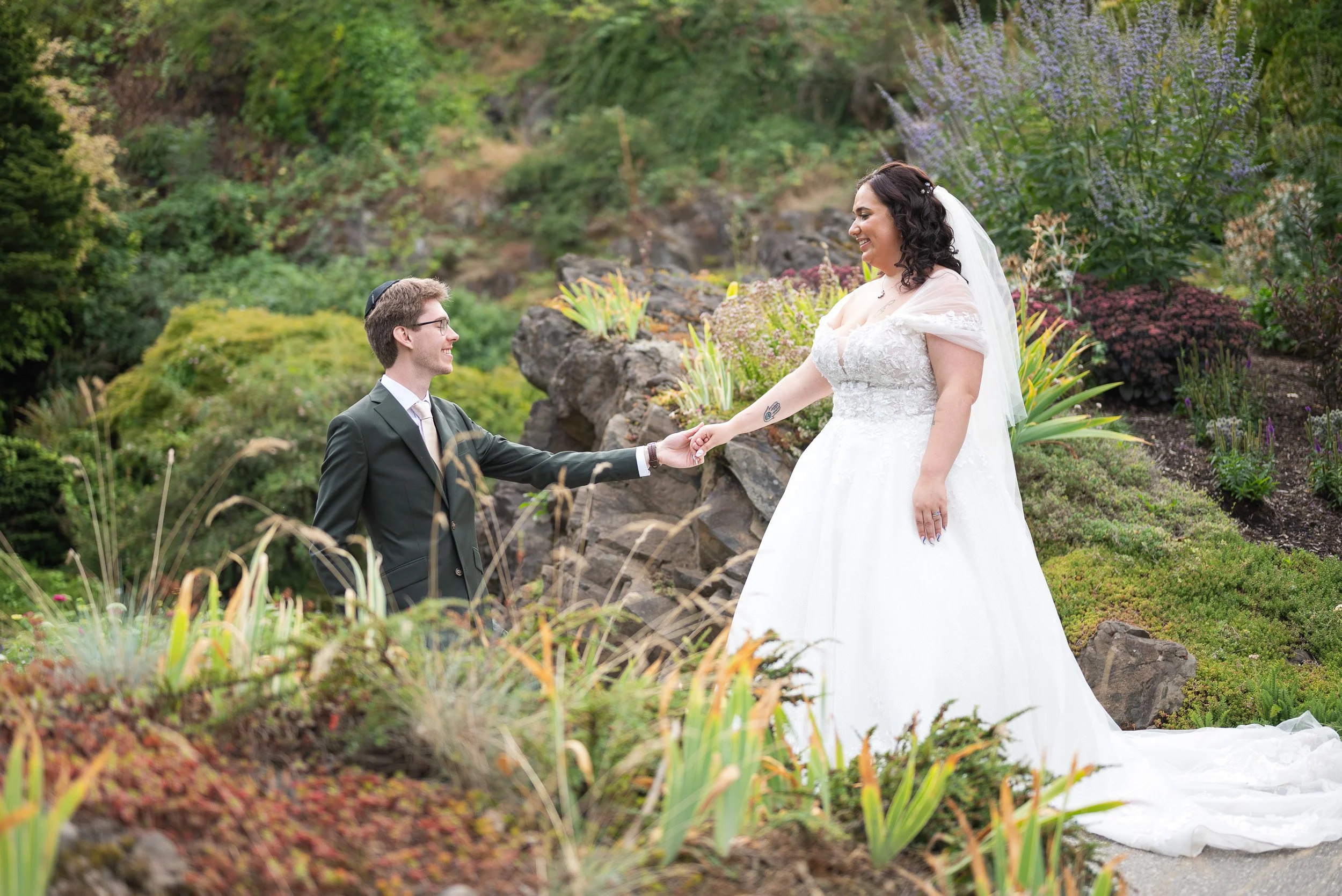 A bride and groom holding hands in a lush garden surrounded by colorful plants and flowers at Queen Elizabeth Park, in Vancouver BC.