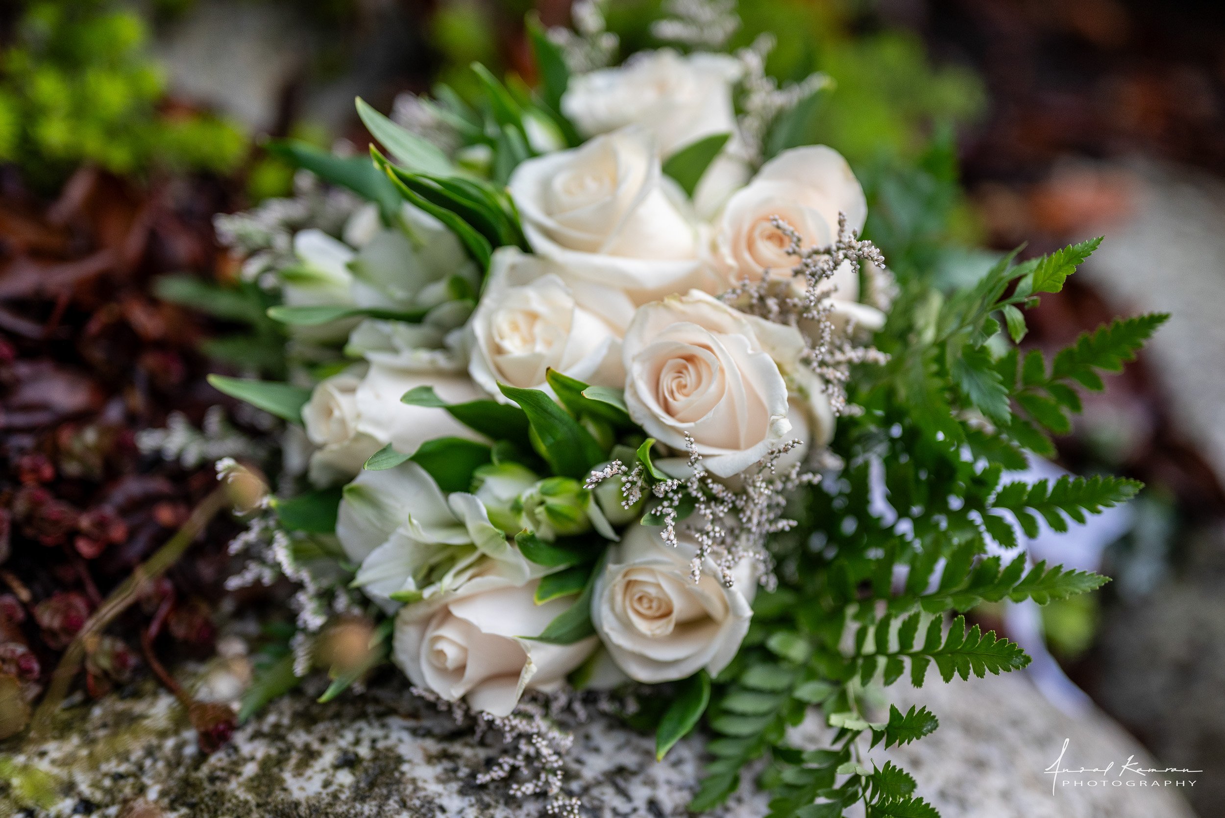 Close-up of a bouquet of white roses and ferns on a mossy surface.