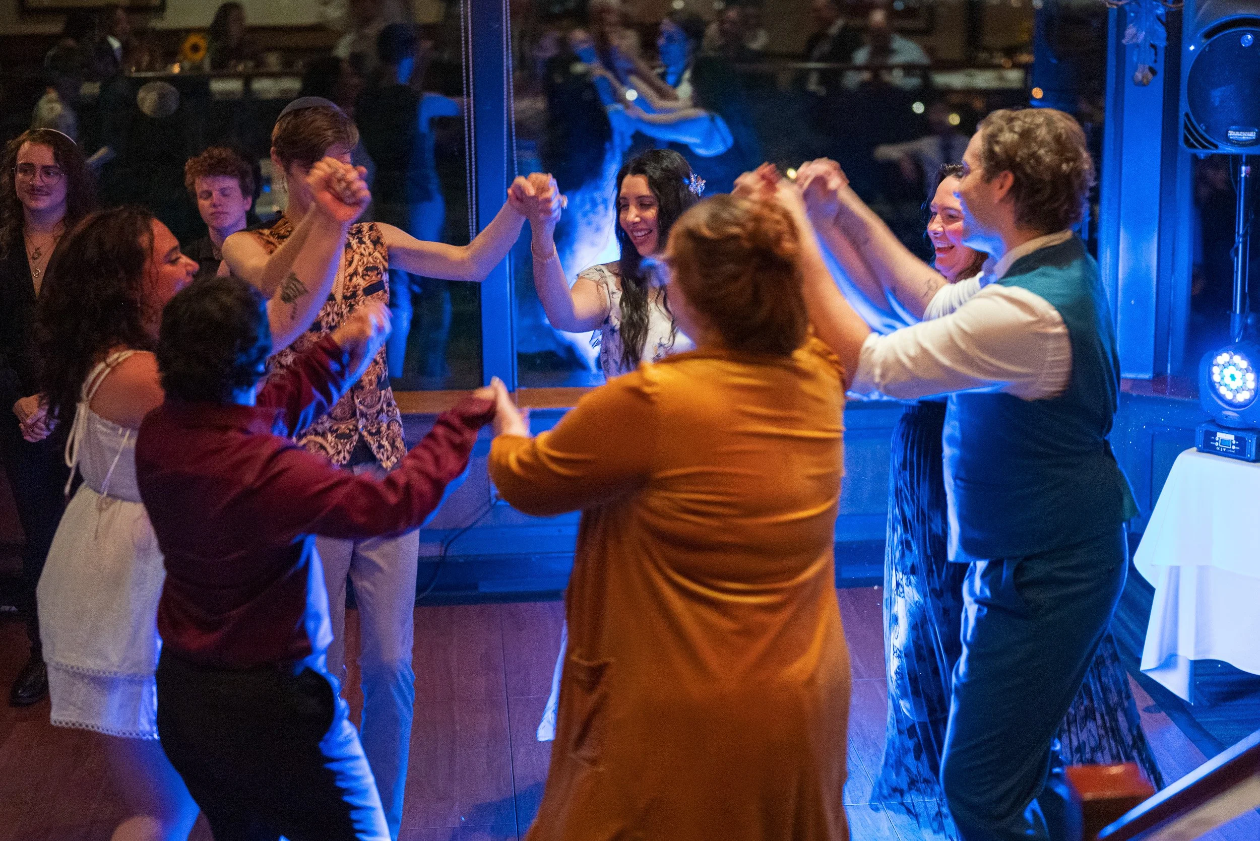 People dancing and celebrating at a party with blue lighting, some holding hands and smiling.