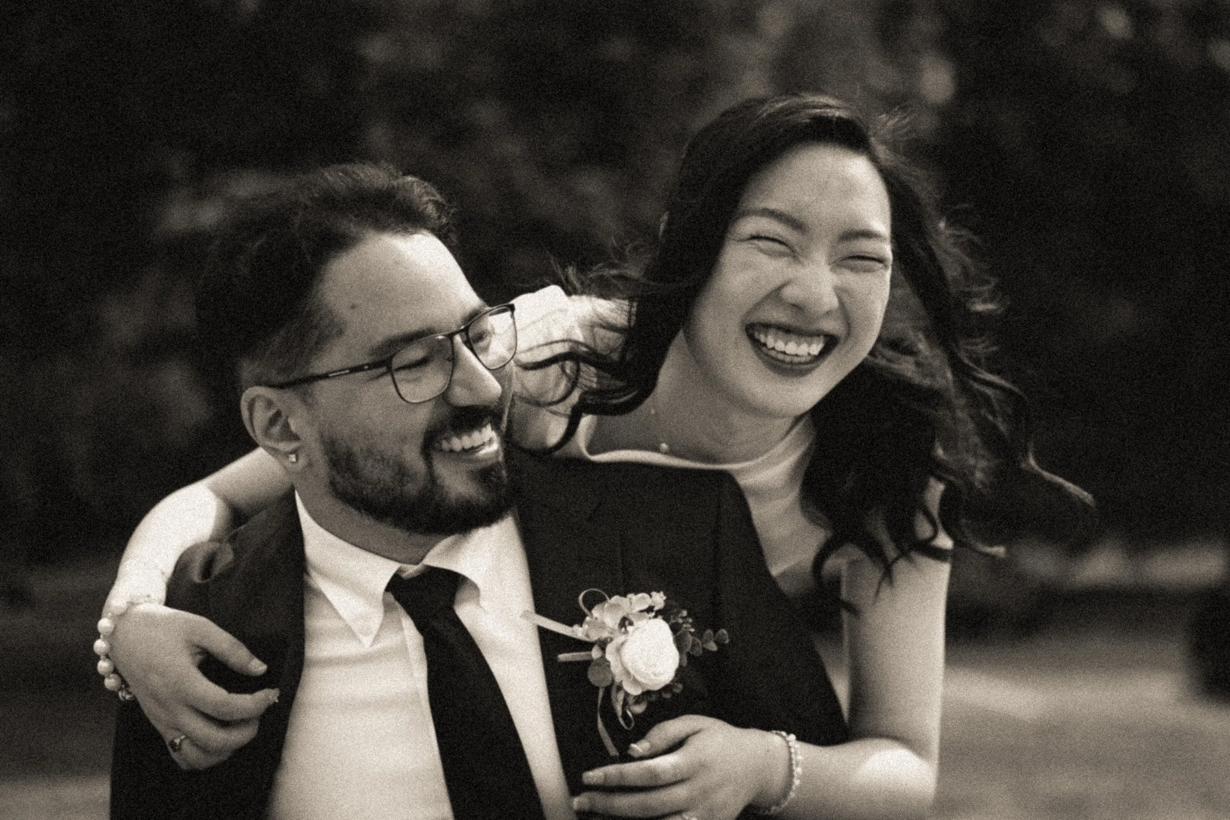 A smiling man and woman in formal attire, possibly at a wedding or celebration, embracing each other with the woman's arm around the man's shoulder.