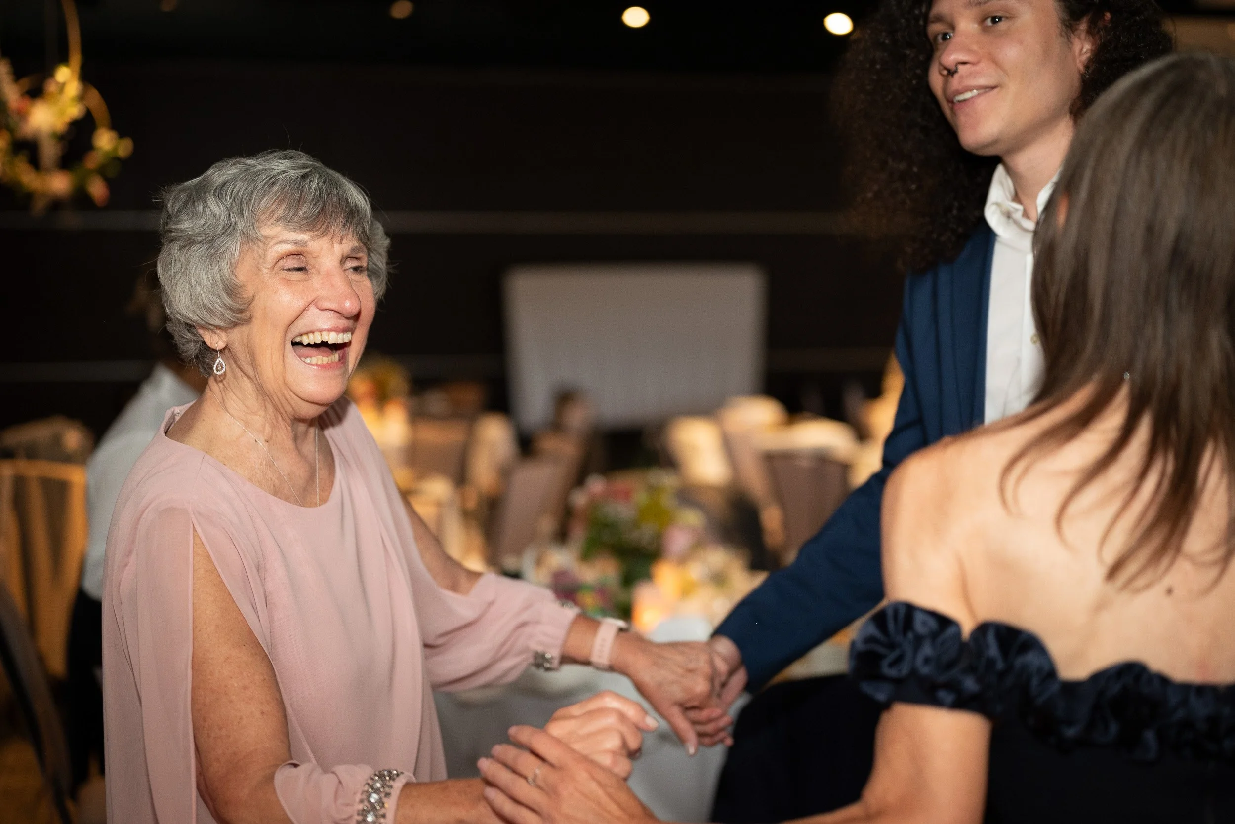 An elderly woman and a younger woman are shaking hands and smiling at each other at a social event.