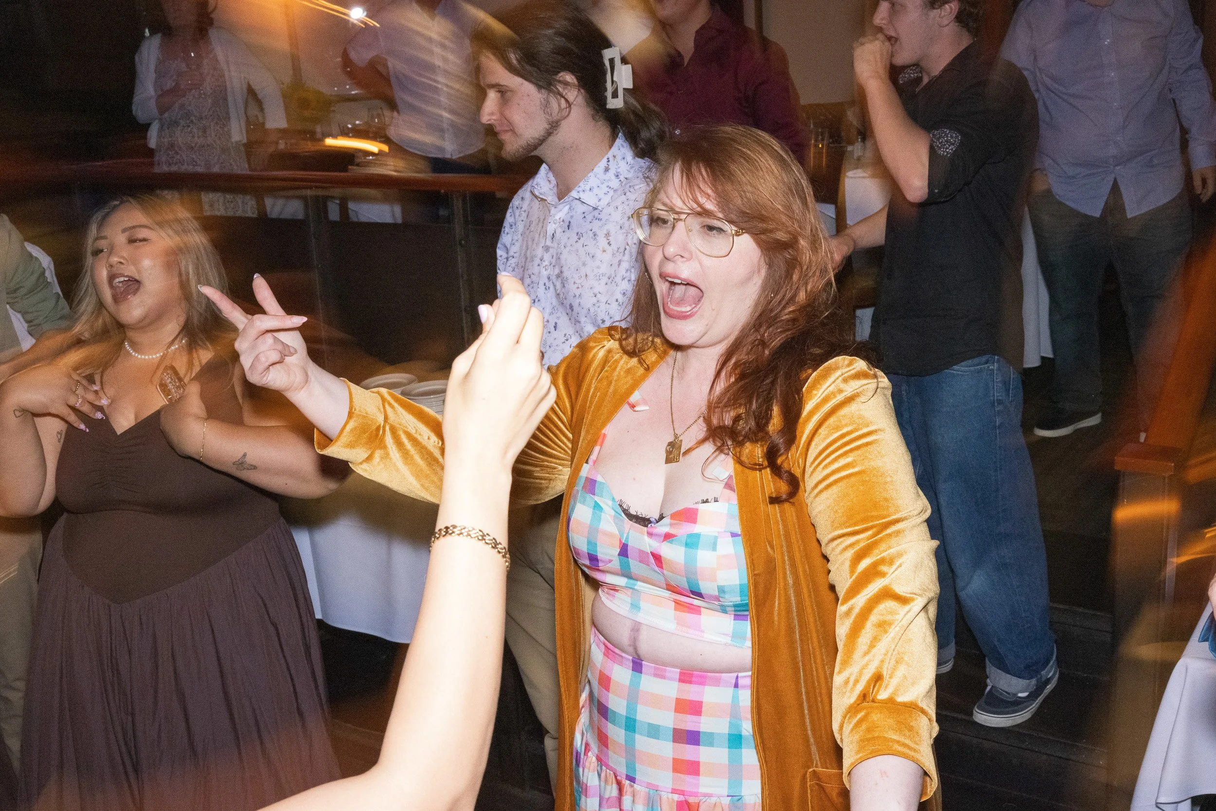A group of people at a party, dancing and having fun, with some individuals singing or shouting, in a lively indoor setting.
