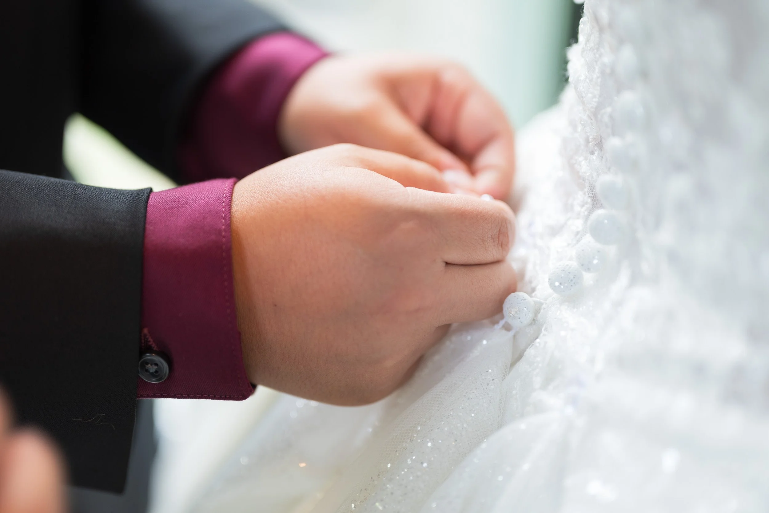 Close-up of a bride and groom's hands holding each other as they walk through soap bubbles during their wedding.