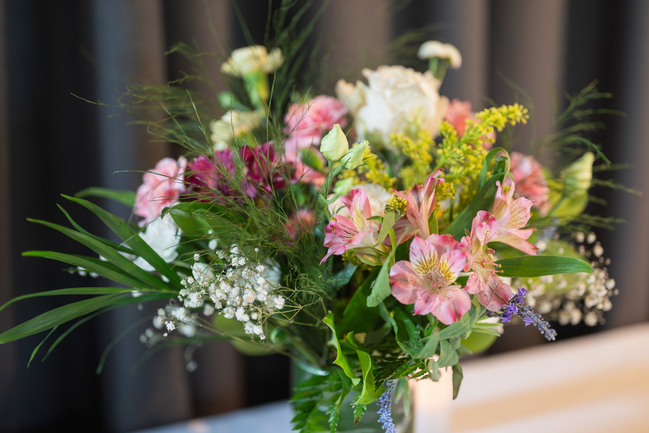 A colorful bouquet of flowers with pink, white, yellow, and purple blossoms in a vase on a dark background.
