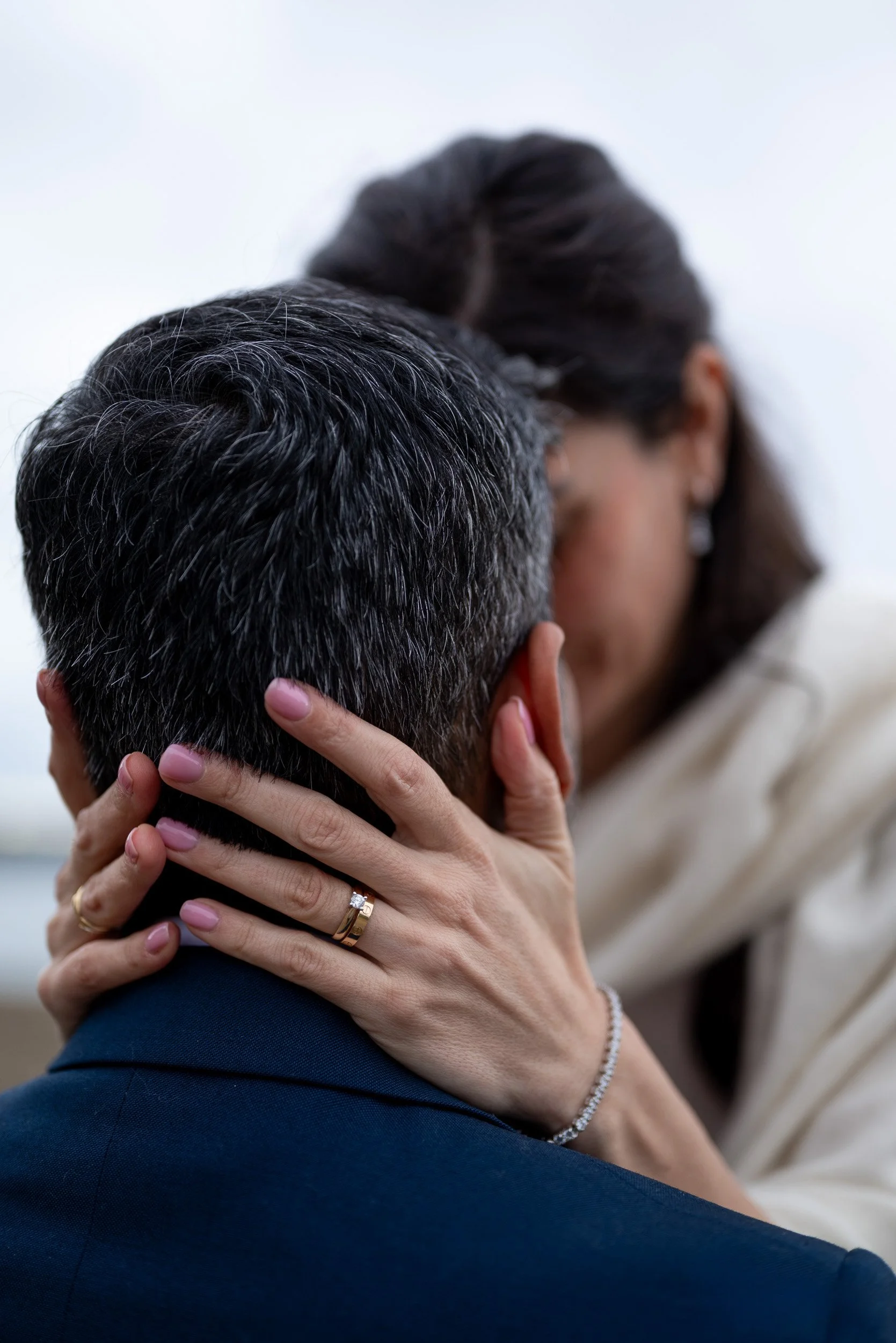 A couple sharing an intimate kiss, with the woman holding the man's face and their hands clasped around each other's necks, highlighting love and affection.