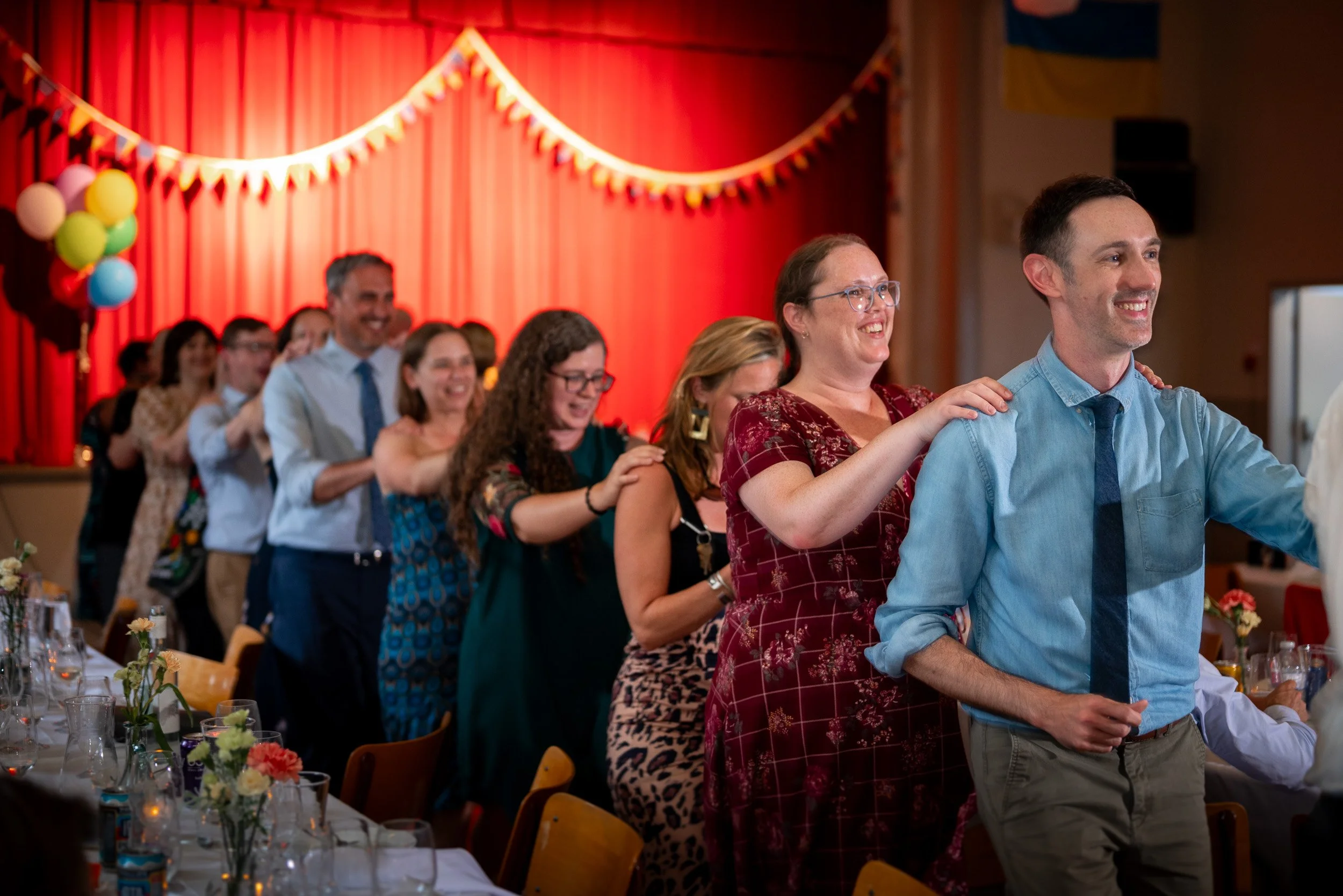 People standing in a line at a celebration or event, with a red curtain and colorful decorations in the background.