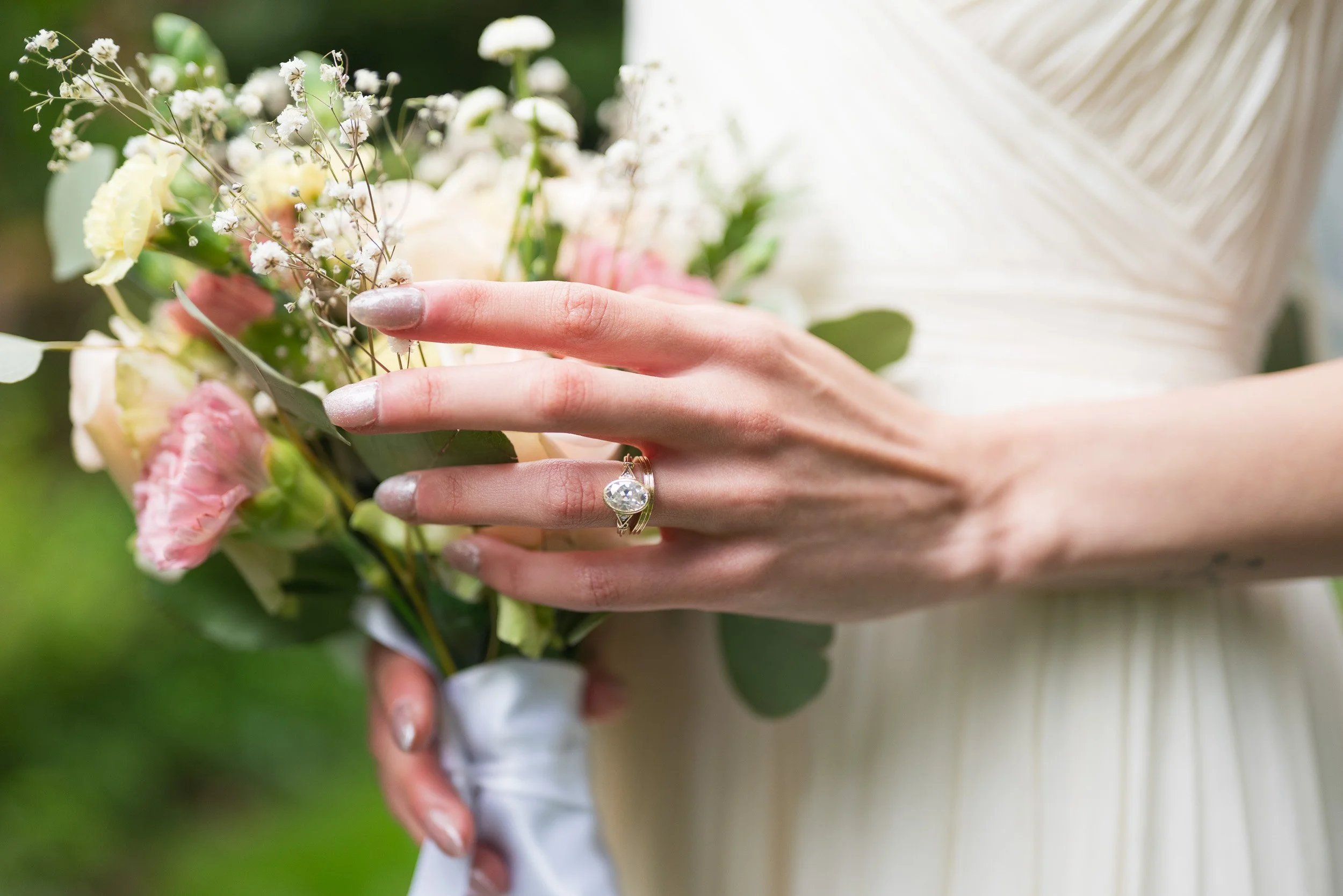 A person in a white dress holding a bouquet of flowers with a diamond ring on their finger.