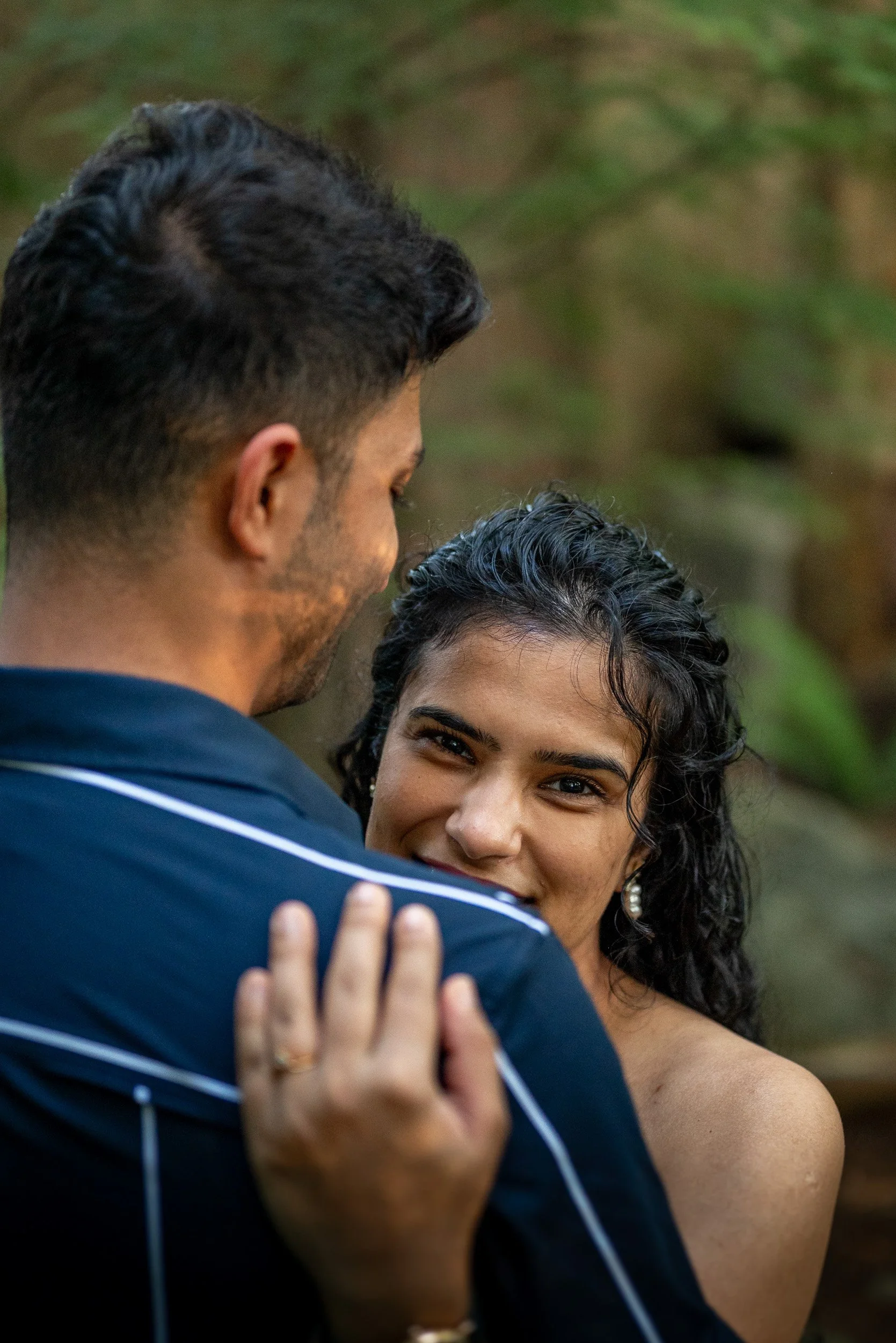 A man and a woman sharing a hug outdoors, with the woman smiling and showing affection.