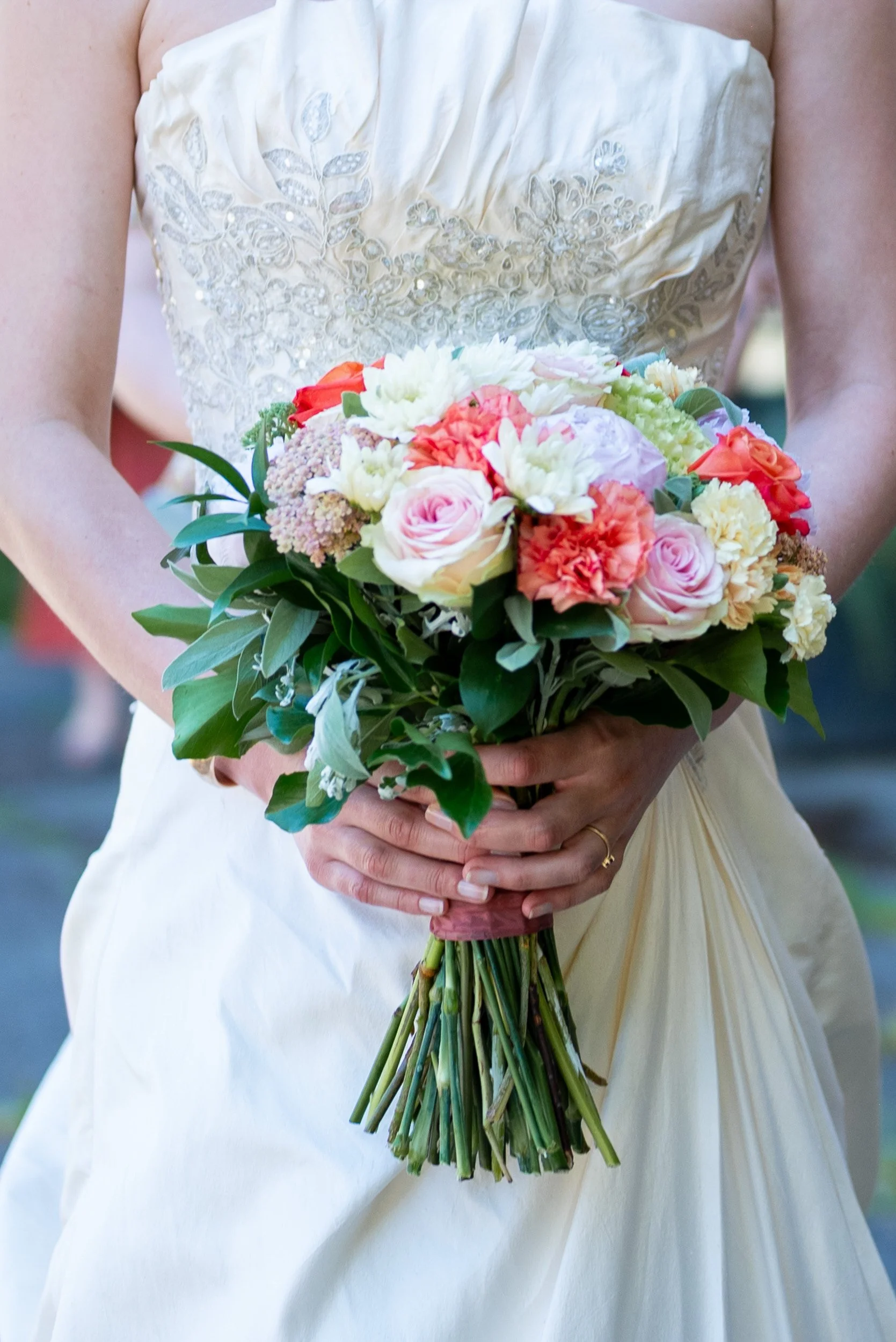 A woman in a wedding dress holding a bouquet of mixed flowers including roses and carnations at her wedding in Vancouver
