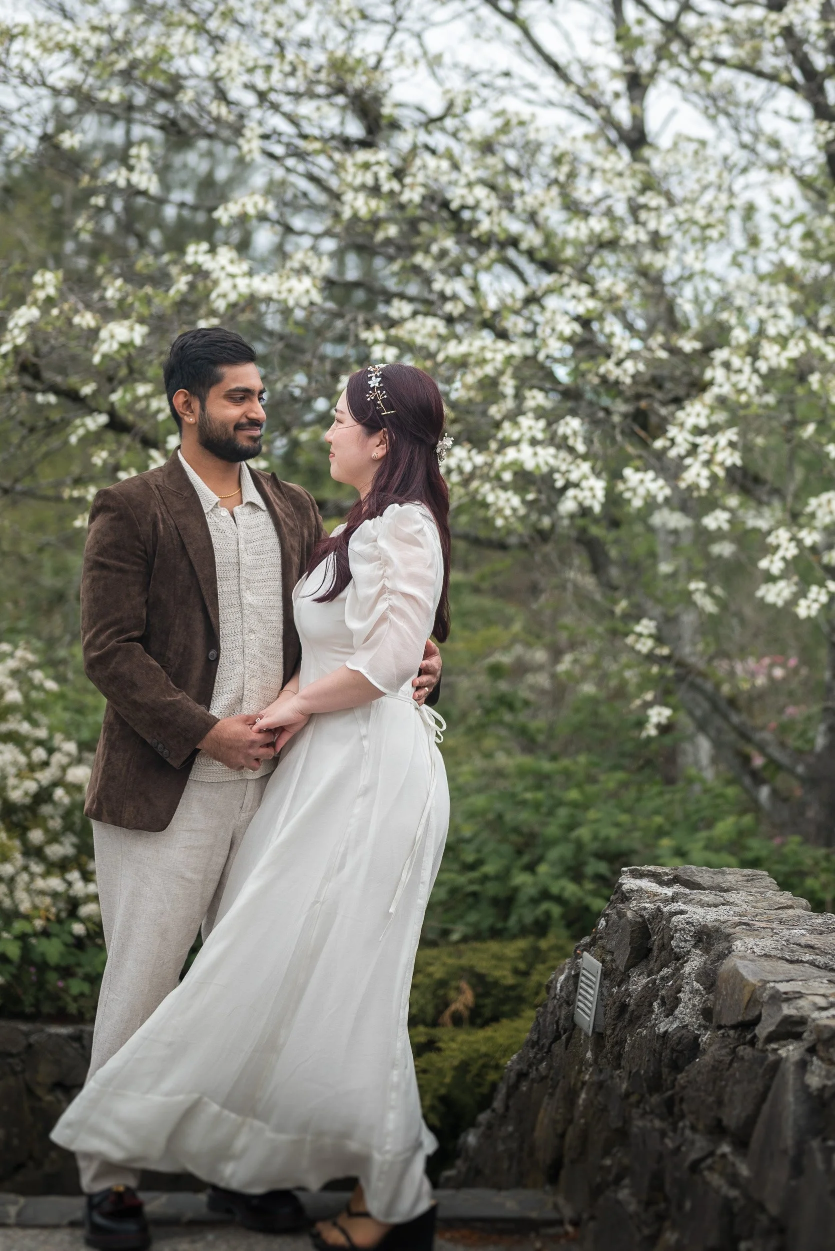 A wedding couple, standing close and looking into each other's eyes outdoors during spring, with cherry blossom flowers in Queen Elizabeth Park.
