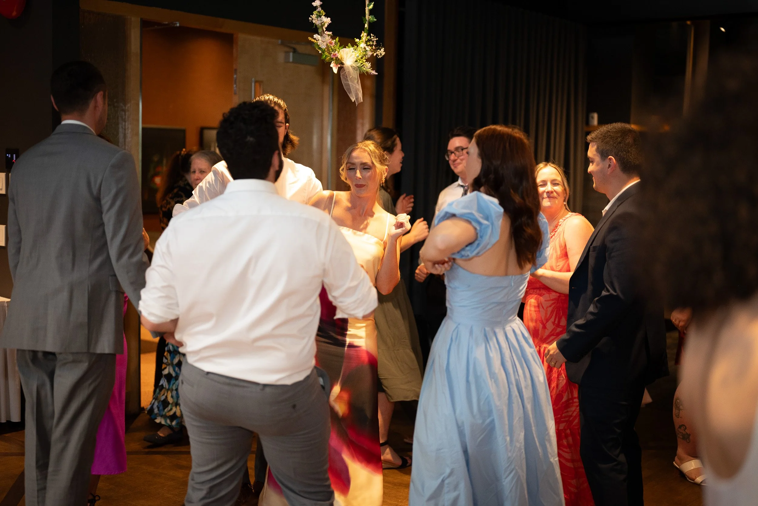 People dancing and socializing at a wedding reception or party, with a floral decoration hanging from the ceiling.