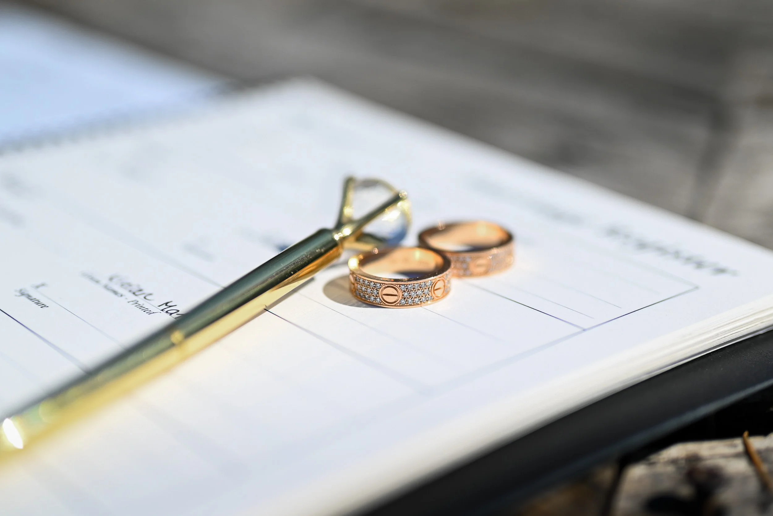 Close-up of two gold wedding rings and a black and gold pen resting on an open document or checkbook with handwritten text.