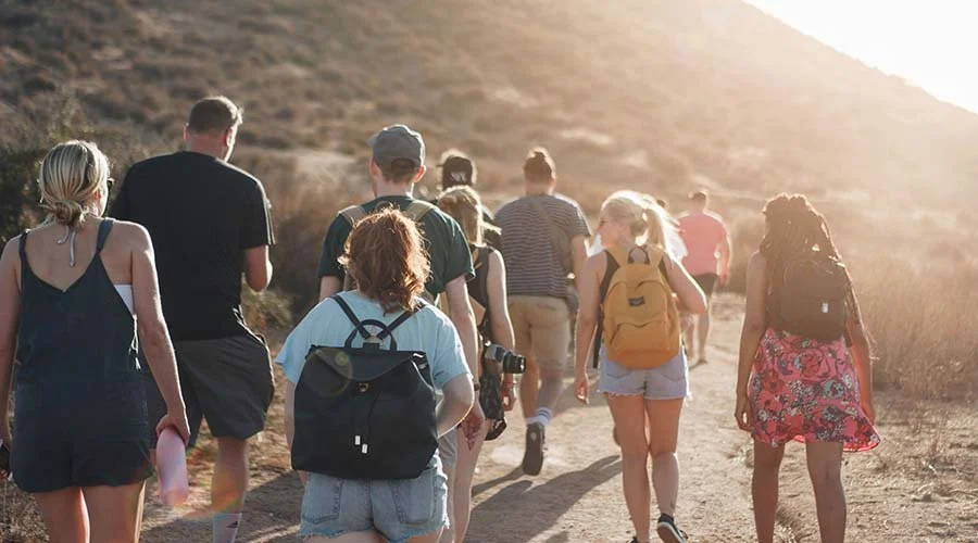 Group of people hiking on a dirt trail in a sunny outdoor landscape.