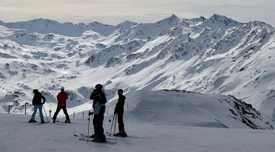 Four people skiing on a snowy mountain with mountain ranges in the background.