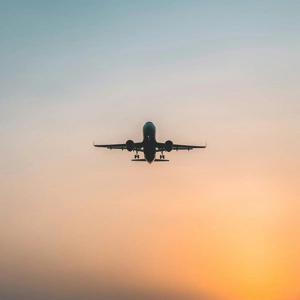 Silhouette of an airplane flying in the sky during sunset or sunrise with a gradient color background.