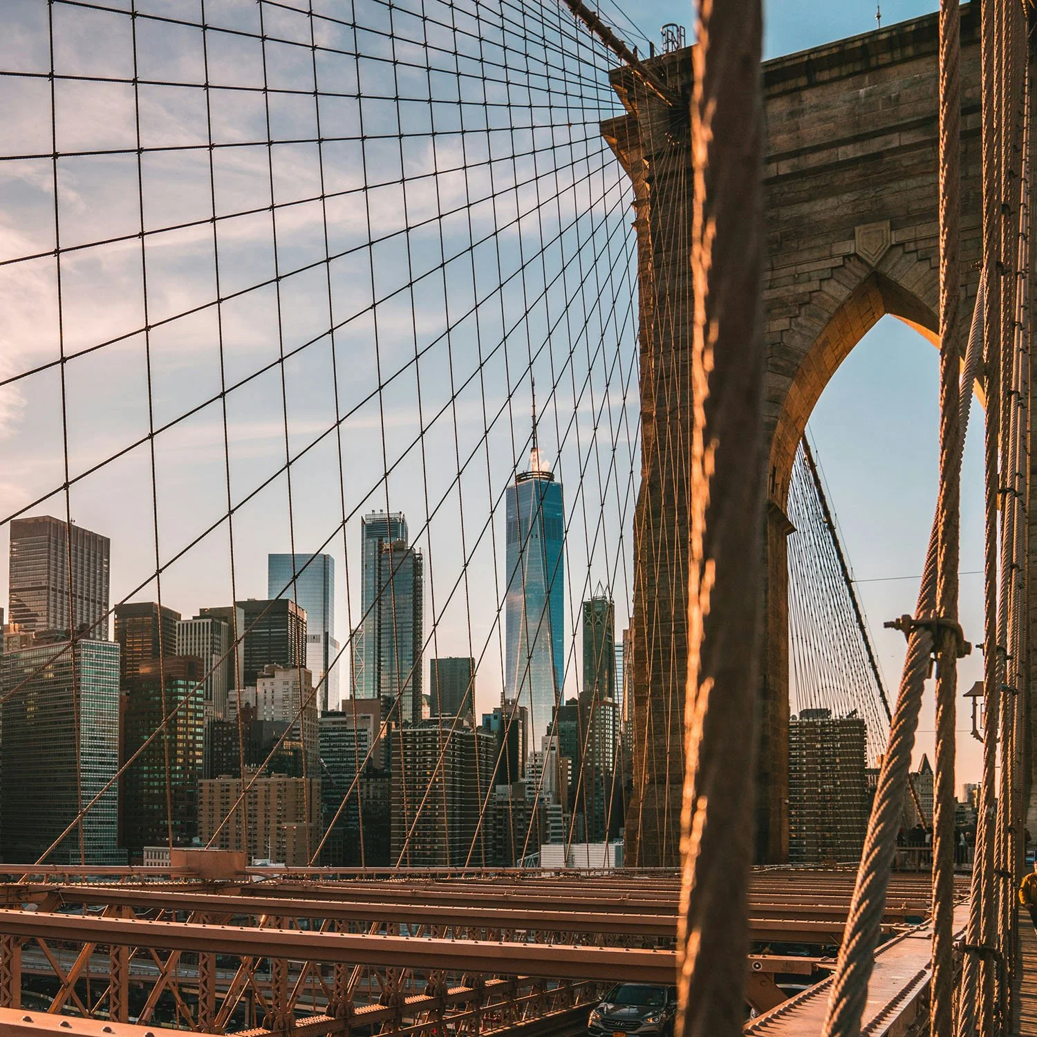 View of New York City skyline through the cables of the Brooklyn Bridge as the sun sets.