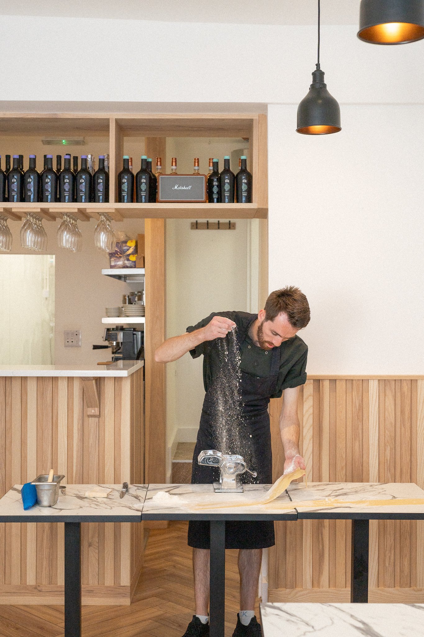 A man in a black chef uniform is making pasta from scratch at a modern kitchen counter.