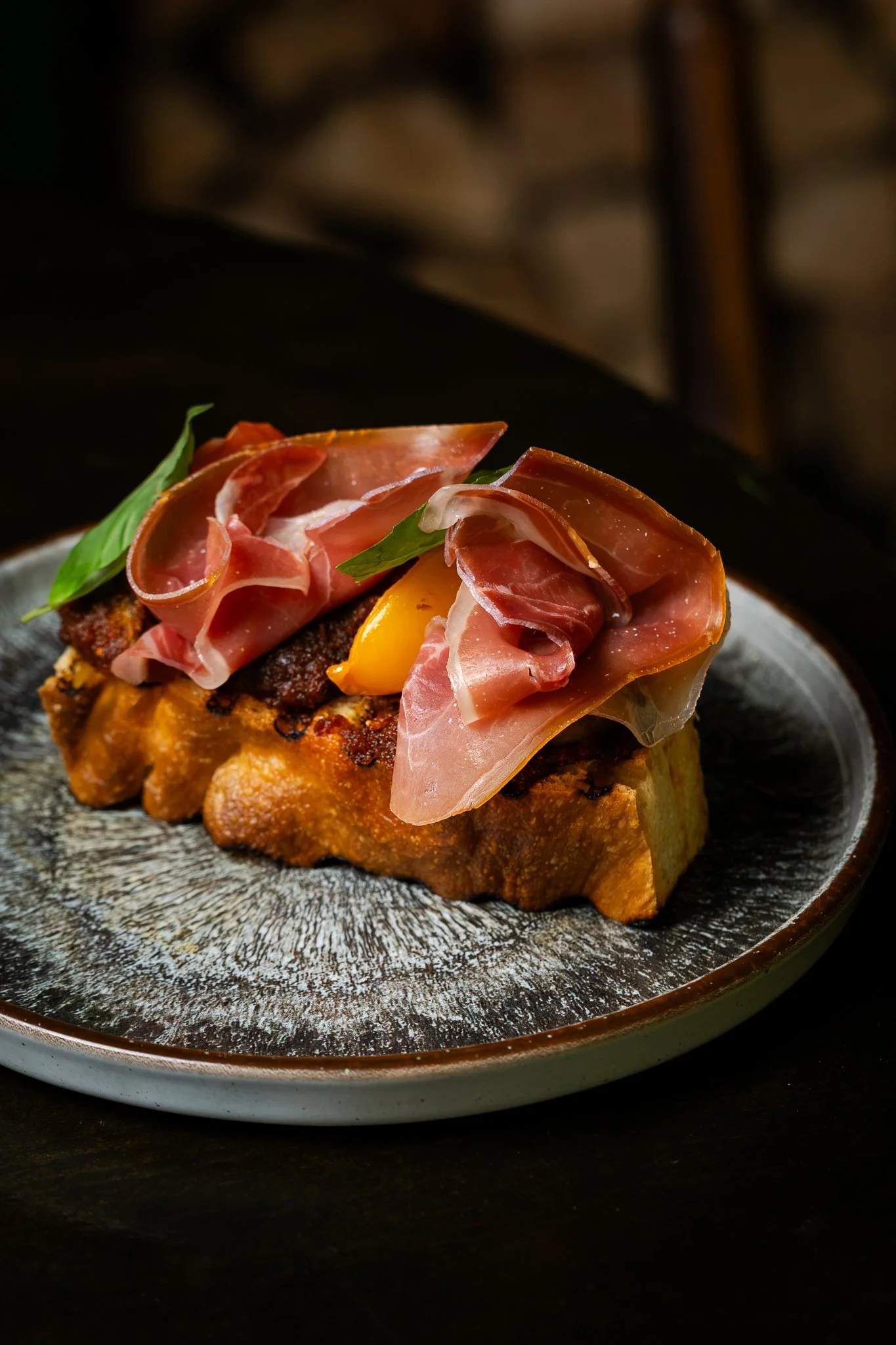 Close-up of a gourmet dish with prosciutto, yellow cherry tomato, basil leaves, served on a rustic ceramic plate.
