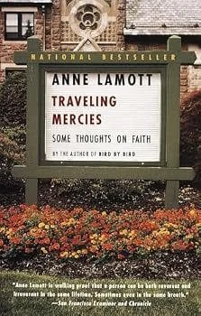 Outdoor bookstore sign advertising Anne Lamott's book Traveling Mercies: Some Thoughts on Faith, with colorful flowers and a brick building in the background.