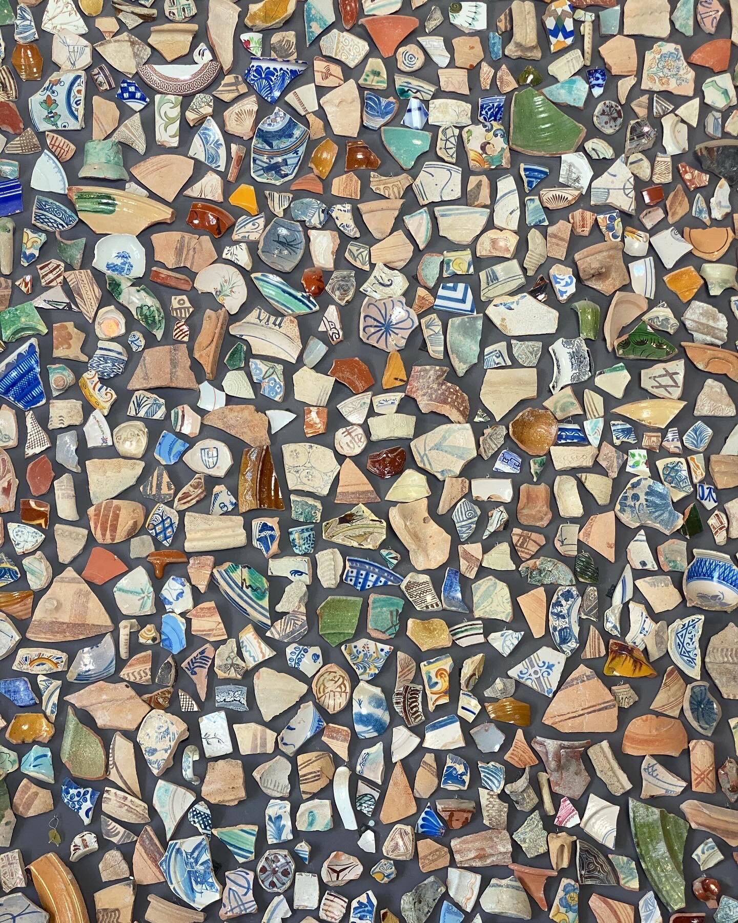 A collection of broken and shattered ceramic and pottery fragments, some decorated with blue, green, yellow, and brown patterns, scattered on a dark background.