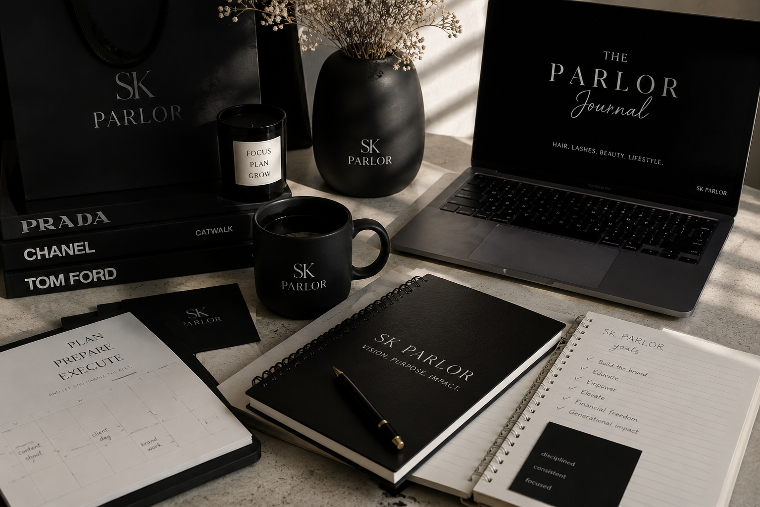 A workspace with SK Parlor branding, including a notebook, planner, mug, candle, and books, displayed on a desk illuminated by sunlight.