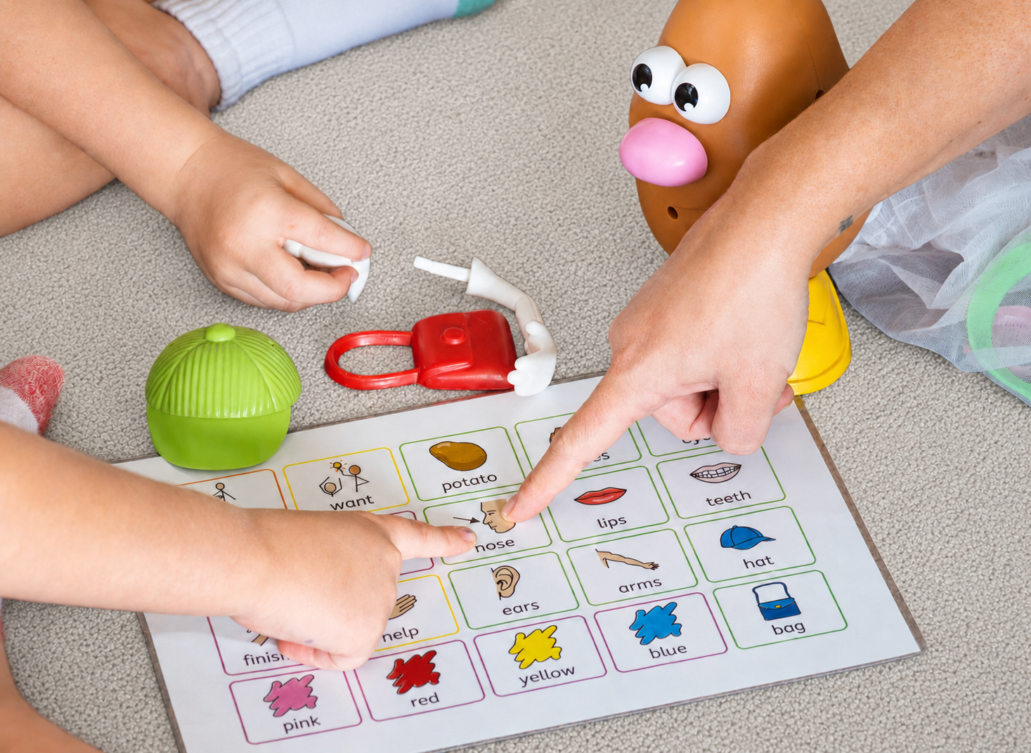 Children playing a word matching game on a carpet floor, with toy accessories and a potato head figure.