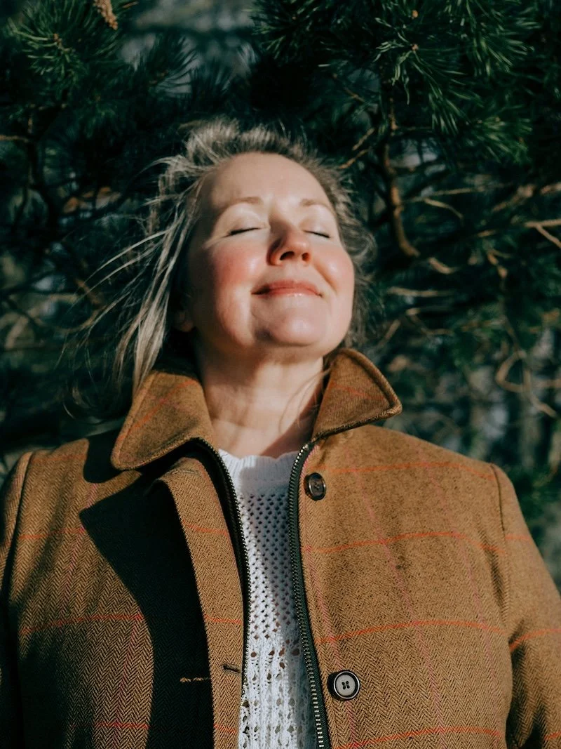 Rev. Bunny Love-Schock in a wool coat with her eyes close and her face to the sun