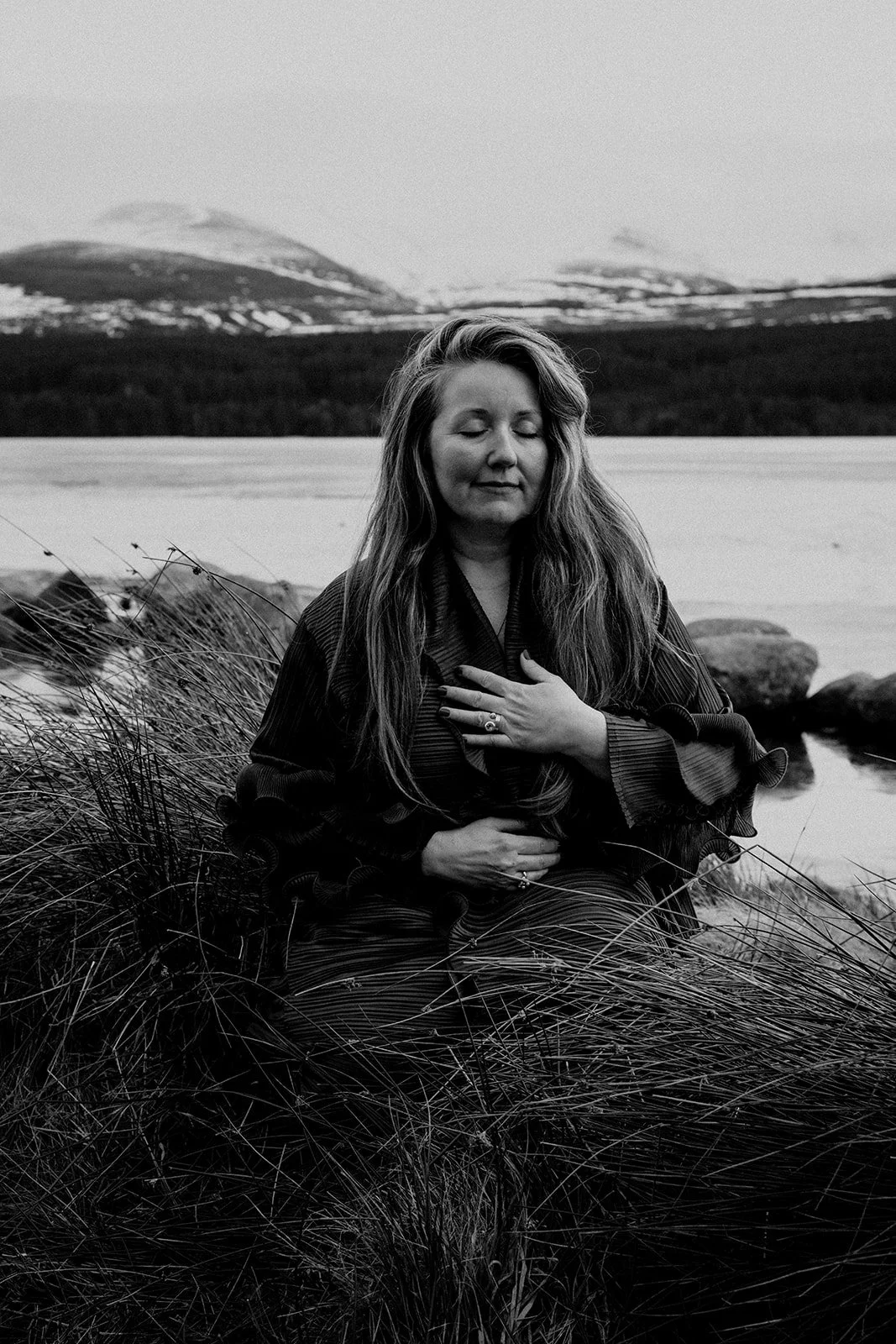 black and white image of Rev. Bunny Love-Schock, sitting by lake in tall grass