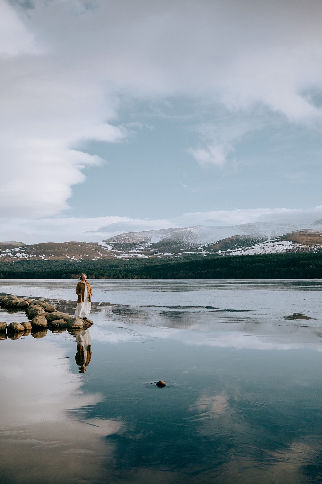 Rev. Bunny Love-Schock standing on the edge of a lake, mountains with snow in the background