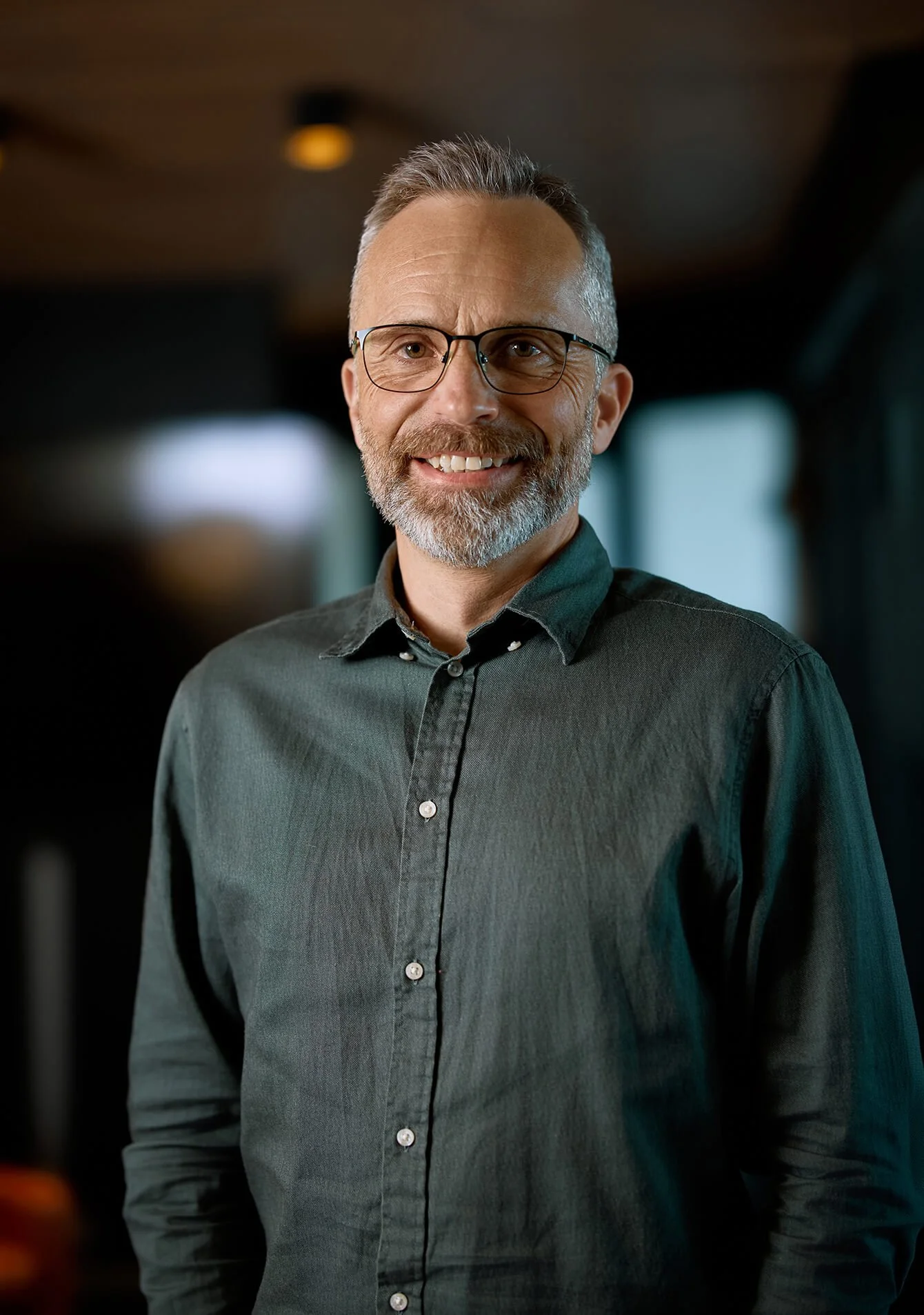 A middle-aged man with glasses and a beard, smiling, wearing a dark green shirt.