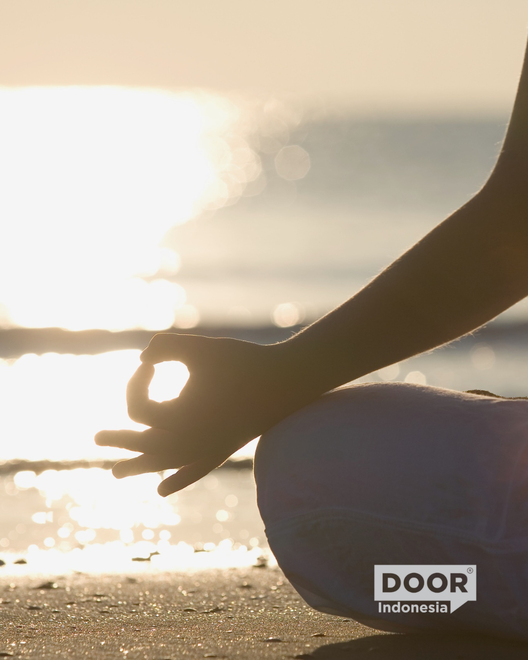 Person meditating on a beach at sunset. DOOR Indonesia logo on the bottom right corner.